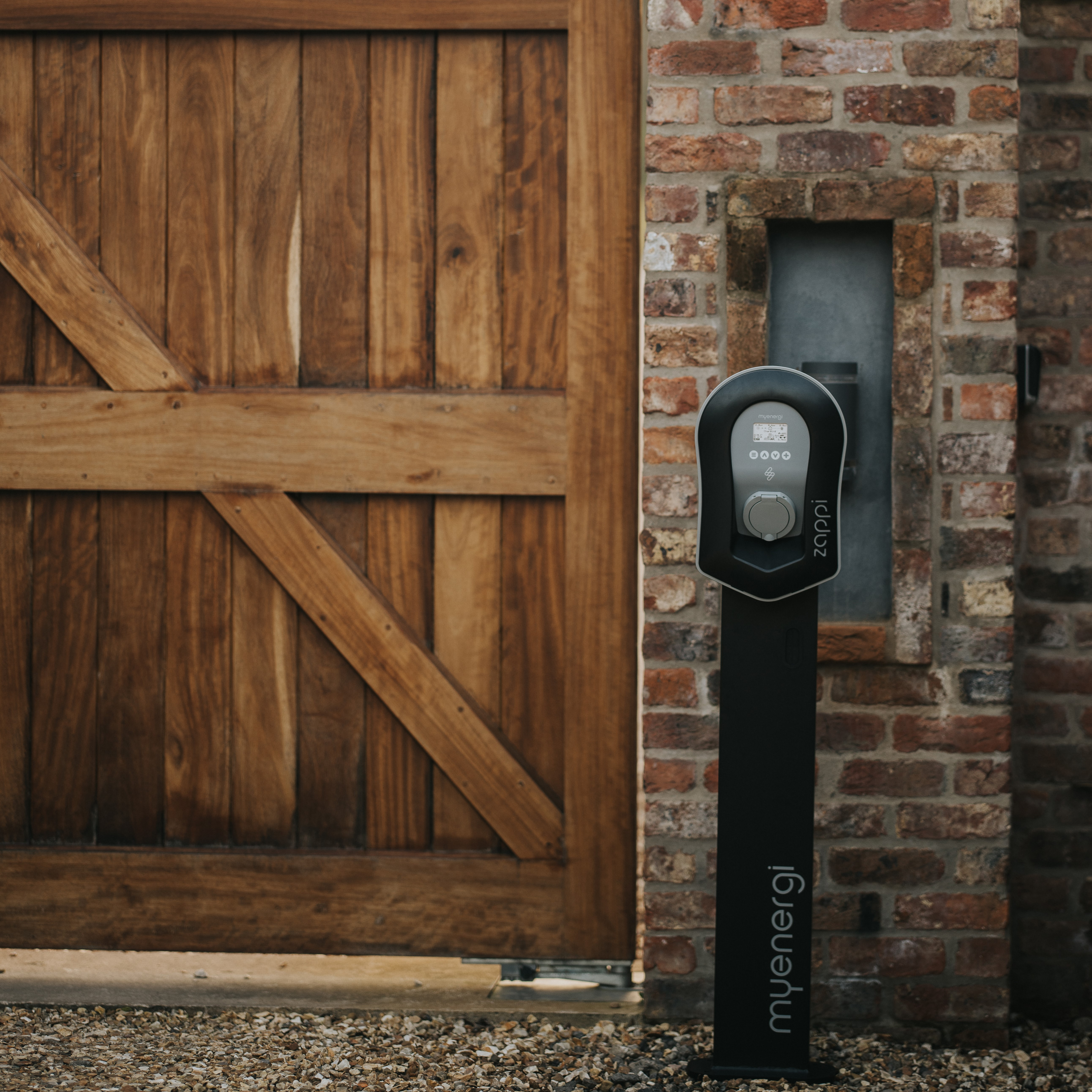 Un caricatore per auto elettriche montato su un muro di mattoni accanto a una porta di legno.