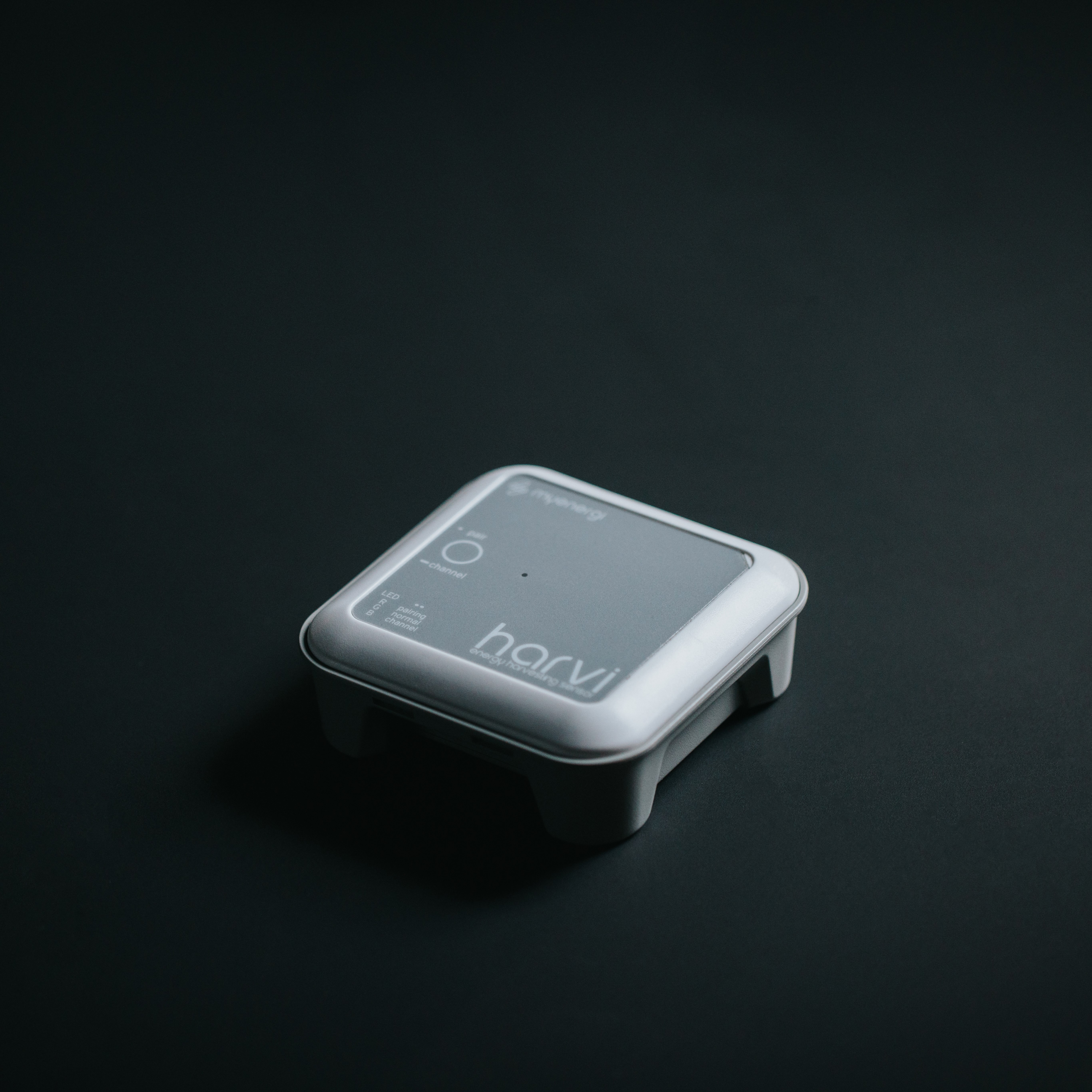 White and gray myenergi harvi device on a dark surface. The device has a logo and button.