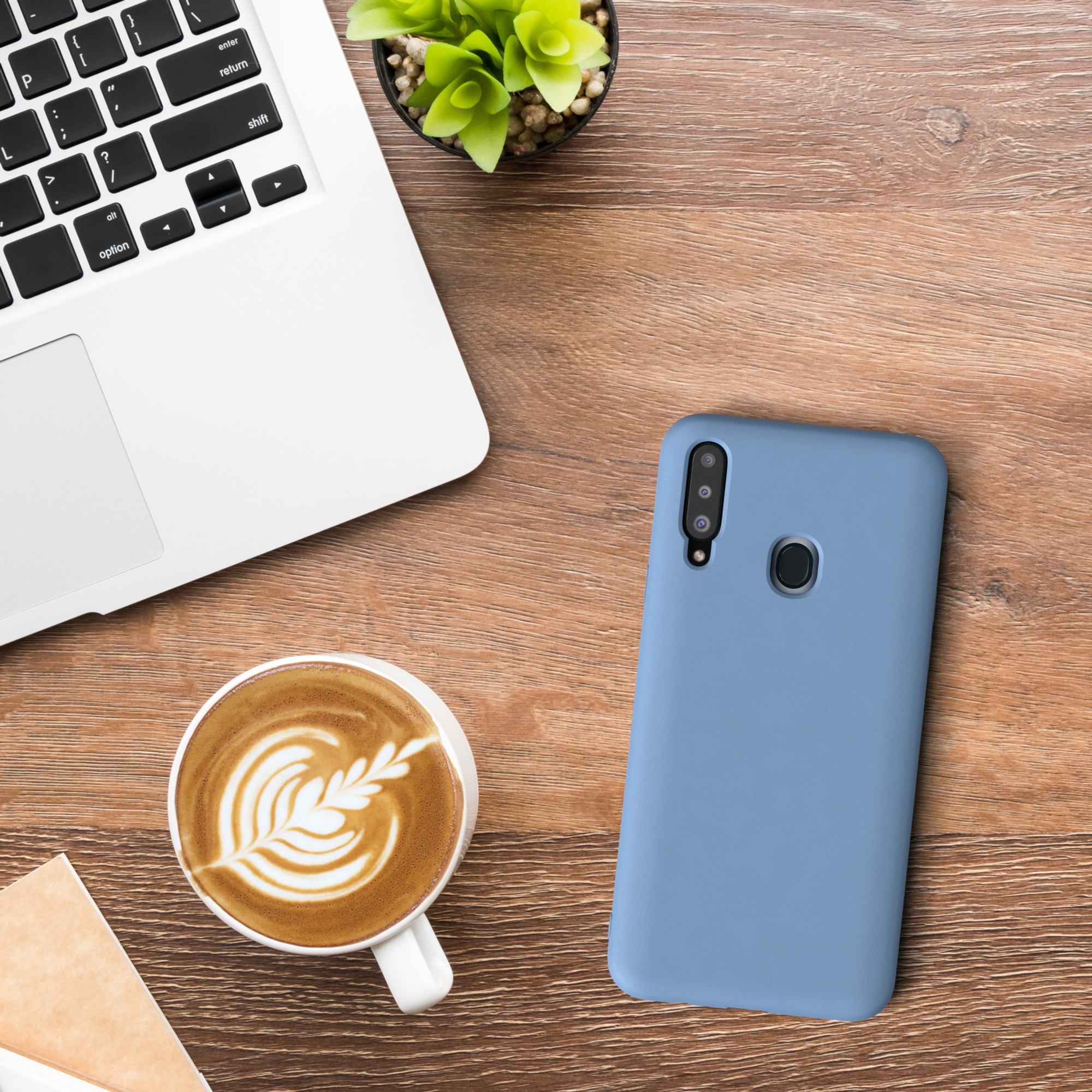Ein Laptop, eine Handyhülle, eine Kaffeetasse mit Latte Art und eine grüne Pflanze stehen auf einem Holztisch.