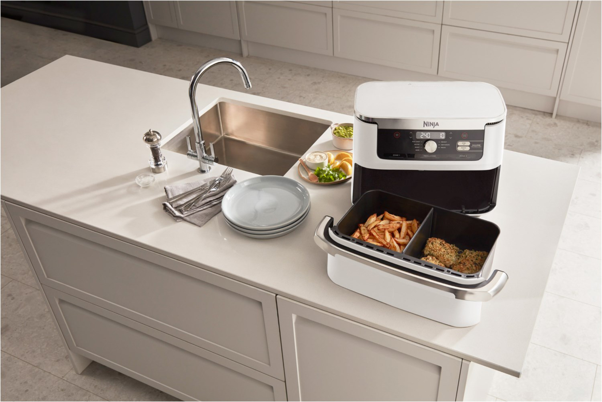 Frytownica powietrzna z jedzeniem. Frytki i burger. Biały blat i zlew w tle.