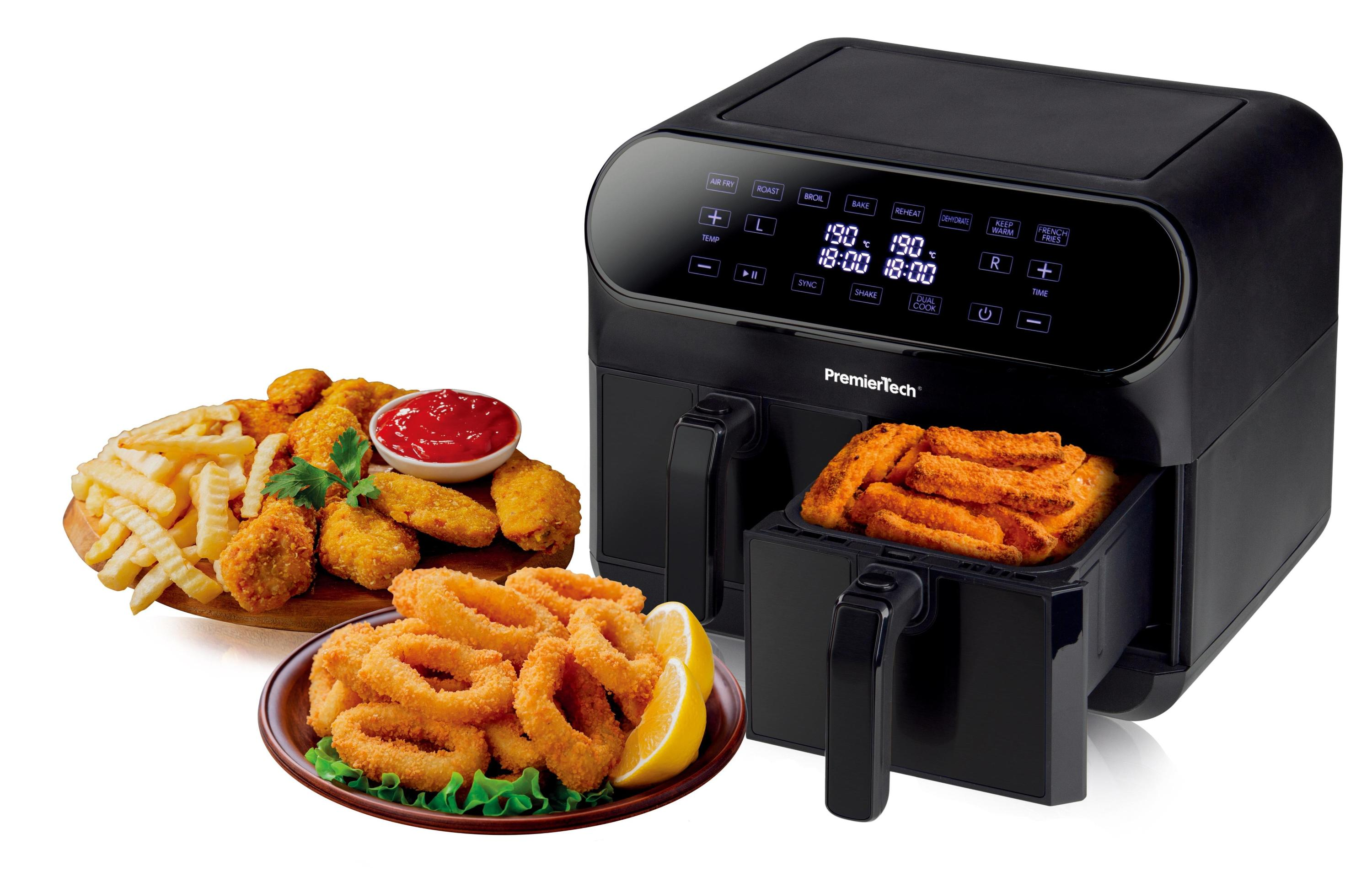 Una friggitrice ad aria nera con cibo all'interno e piatti di cibi fritti: patatine fritte, nuggets e anelli di cipolla.