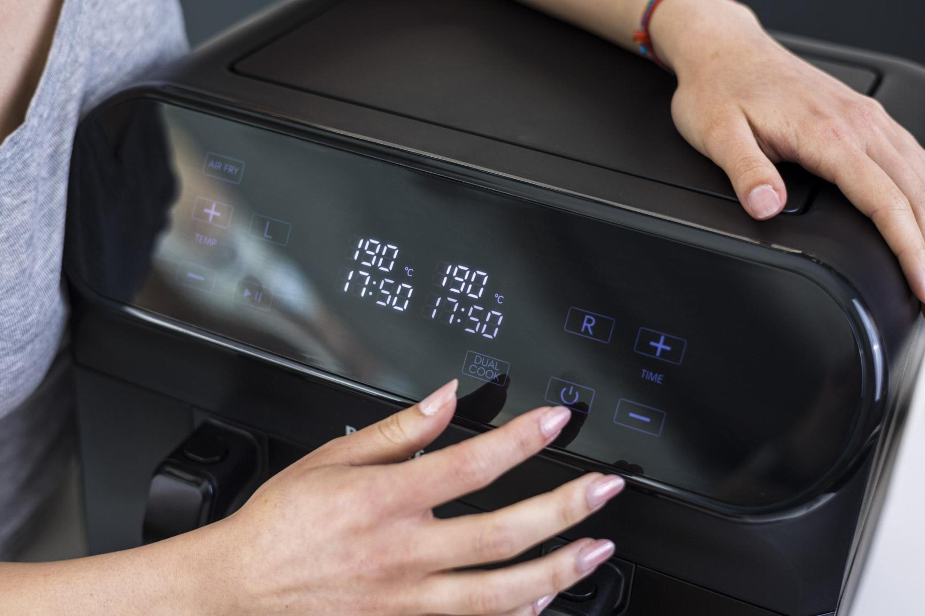 Mani di una persona su una friggitrice ad aria nera, con display digitale.