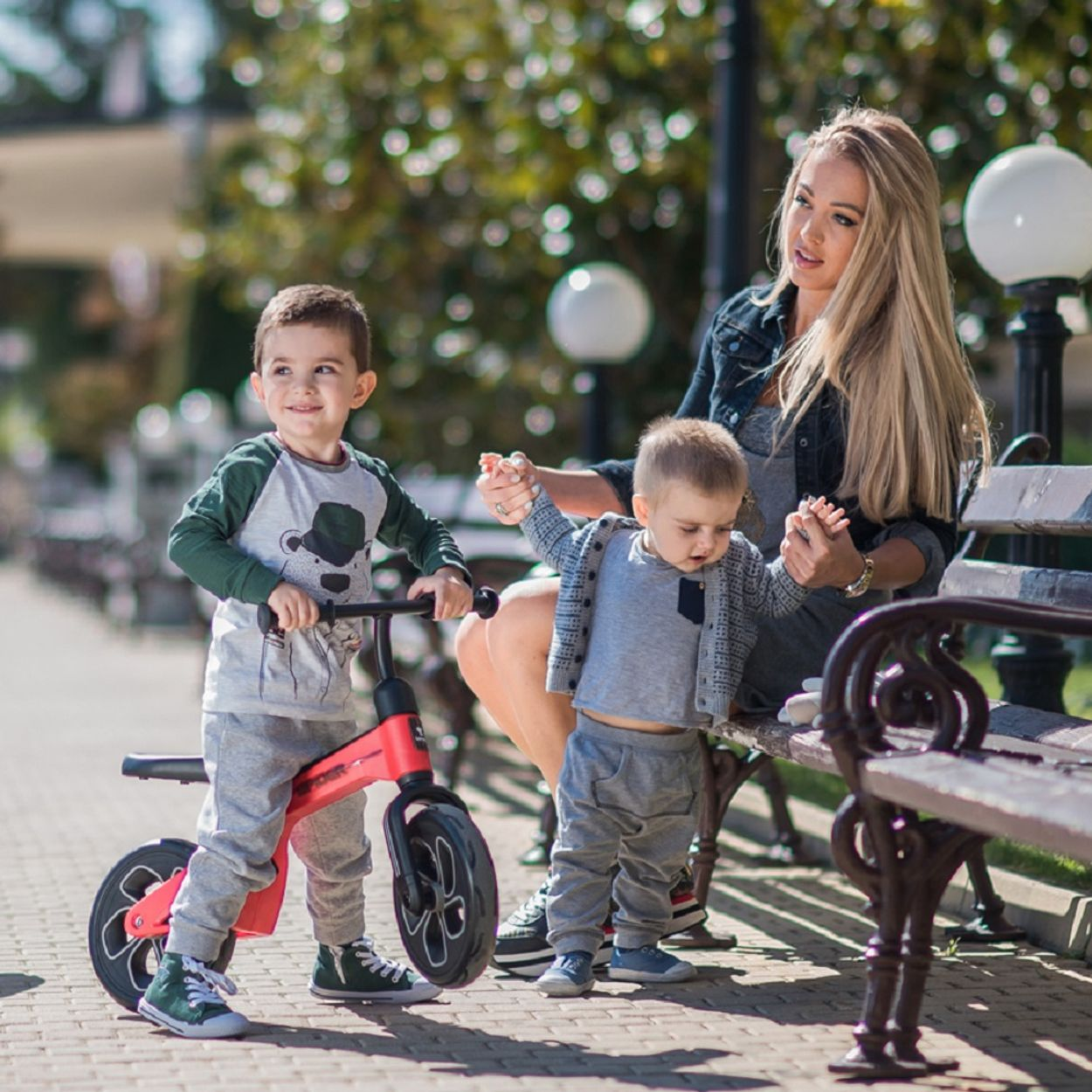 Eine Frau sitzt auf einer Bank mit zwei kleinen Kindern. Eines fährt Fahrrad.