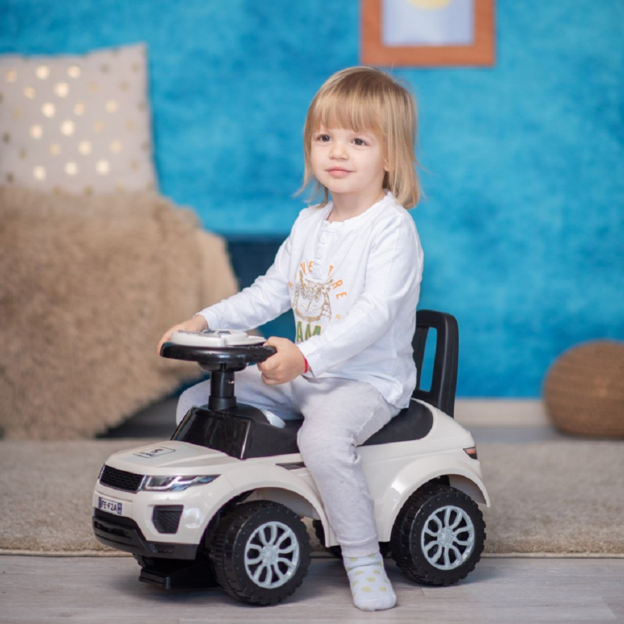 Niño pequeño conduciendo un coche de juguete. Coche blanco, fondo azul.