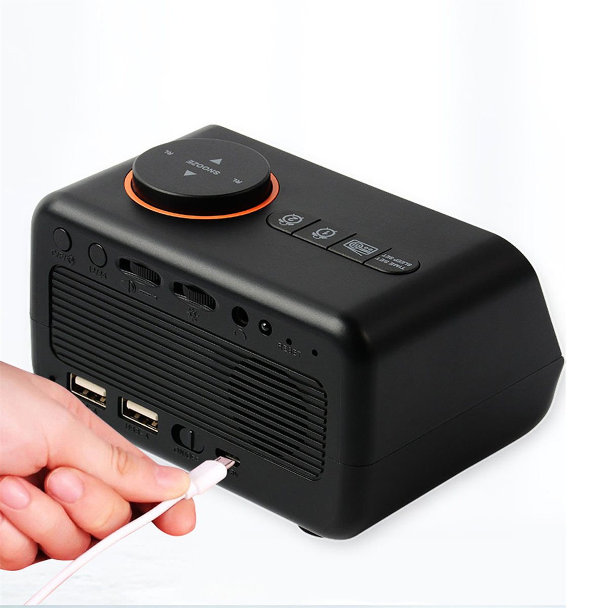 Schwarzer digitaler Wecker mit orangefarbenen Akzenten, eine Hand steckt ein Ladekabel ein.