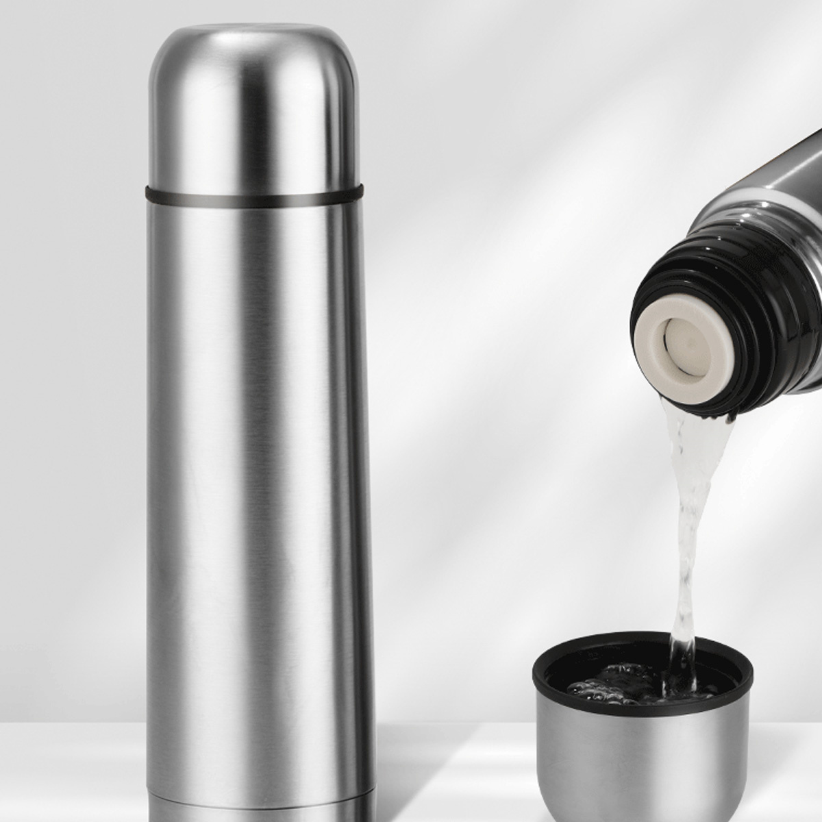 Silberne Thermoskanne, Wasser wird in eine Tasse gegossen.