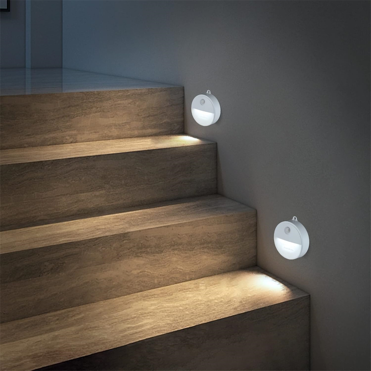 Zwei weiße, kreisförmige LED-Leuchten an einer grauen Wand über Holztreppen montiert.