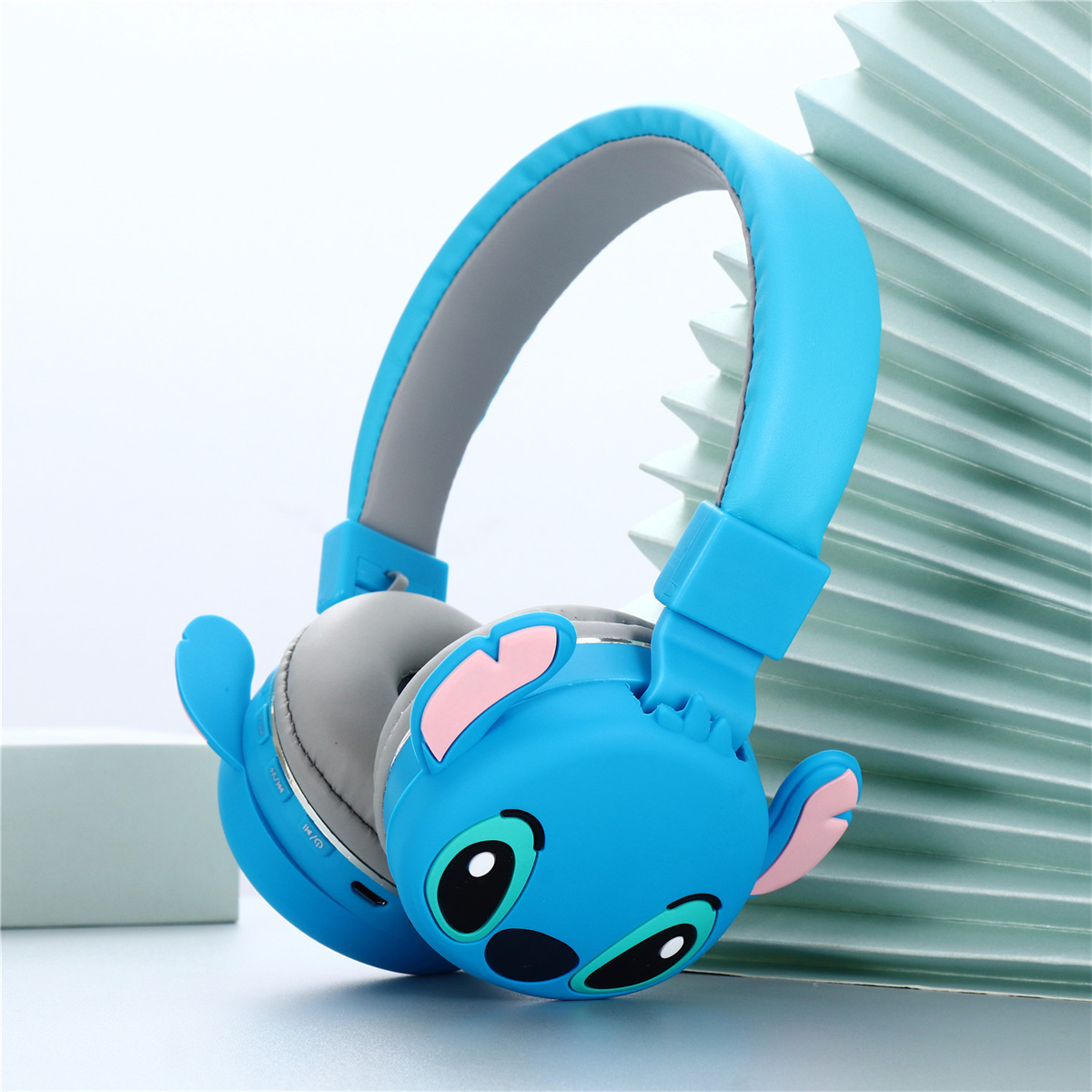 Blaue Stitch-Kopfhörer mit Stitch-Gesicht auf den Ohrmuscheln, auf hellblauem Hintergrund.