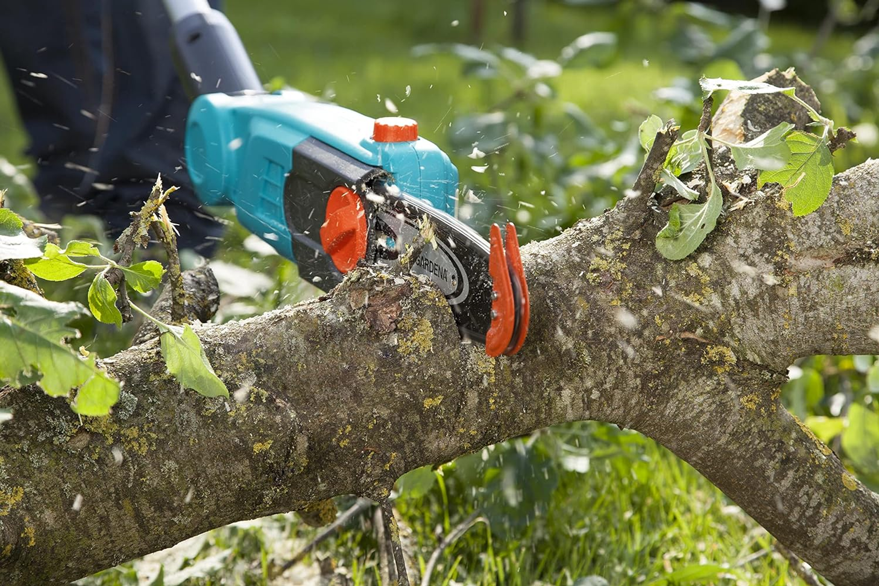 Sega a catena elettrica che taglia un ramo, con trucioli di legno ed erba verde.