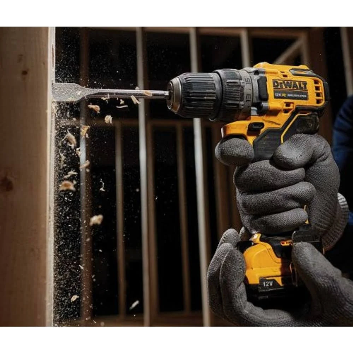 Osoba używa żółto-czarnej wiertarki DeWalt na drewnie, z wiórami.