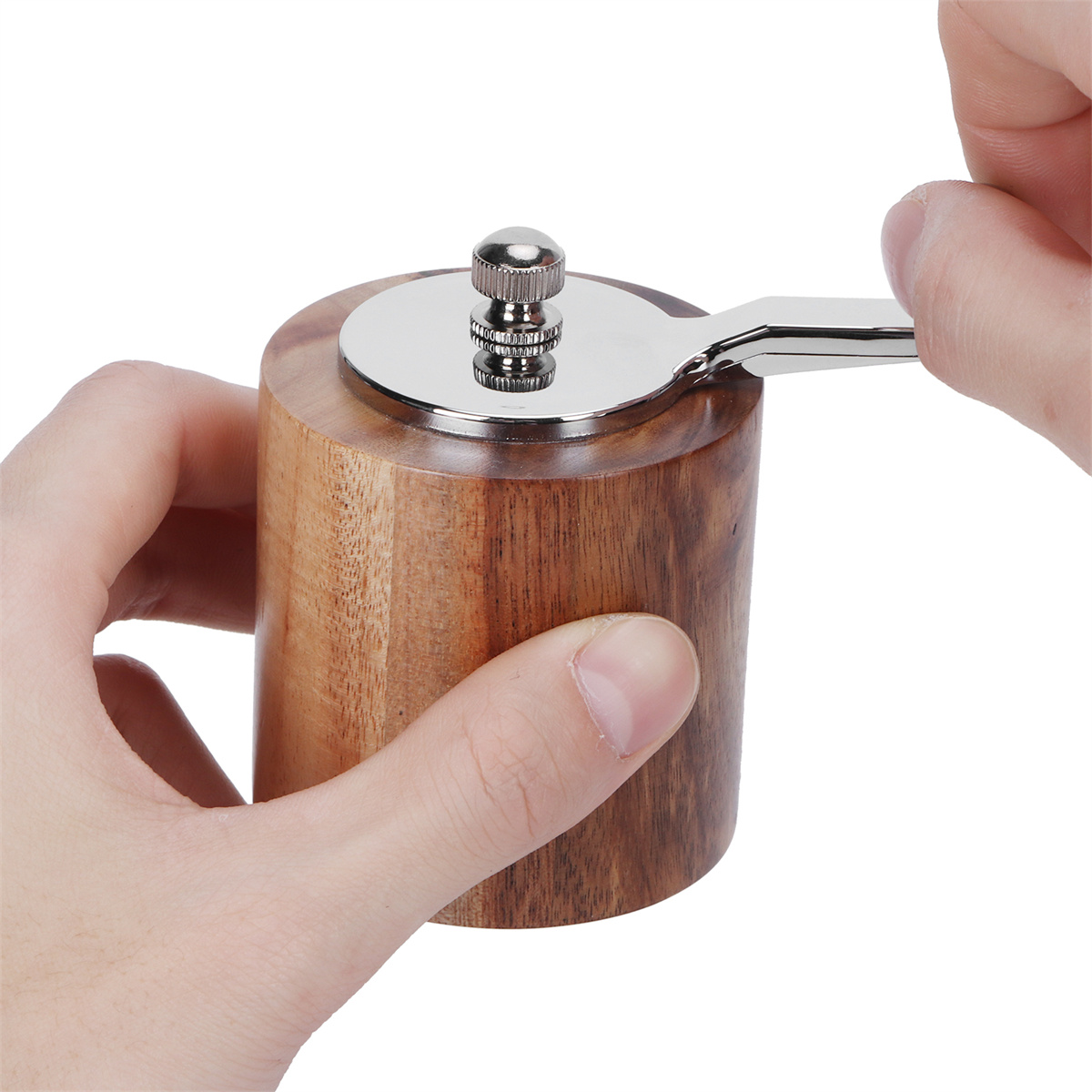 Ein hölzerner Pfeffermühle, die von zwei Händen benutzt wird. Der Hintergrund ist weiß.