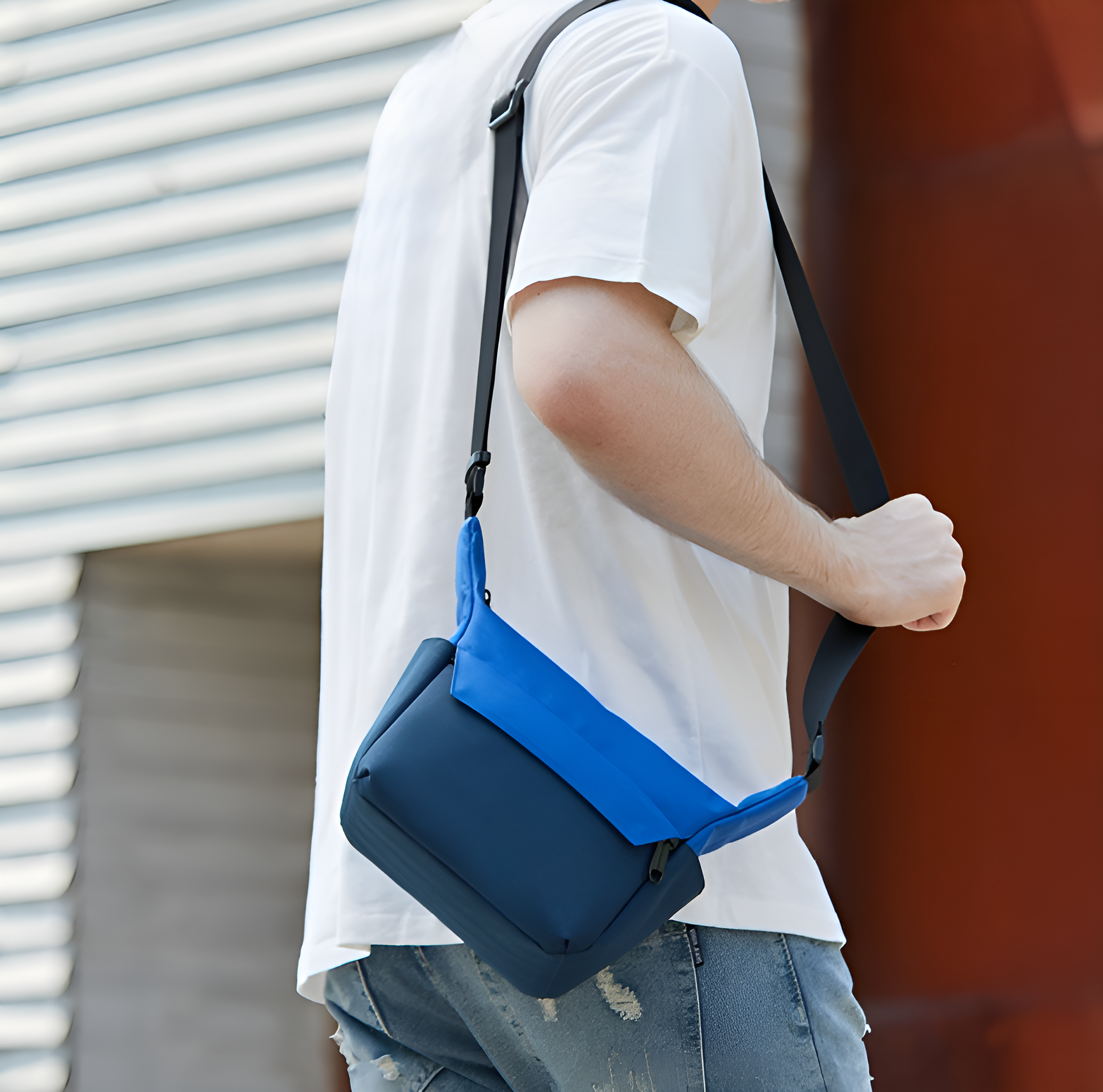 Mann mit blauer Umhängetasche, geht draußen, sonniger Tag.