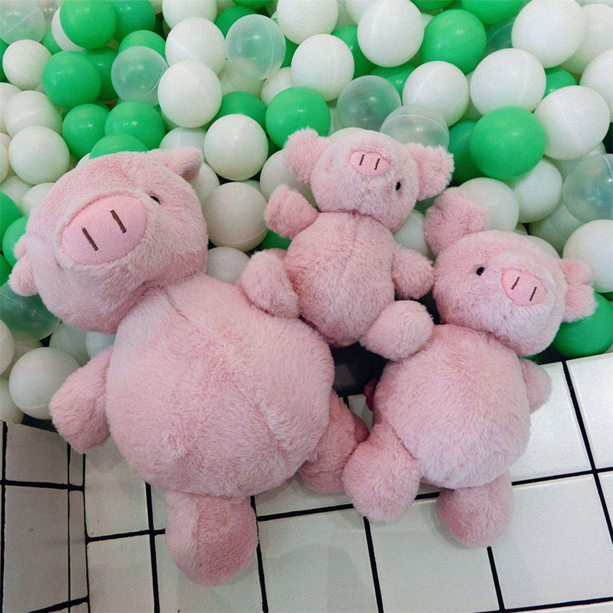 Drei rosa Plüschschweinchen mit weißen und grünen Bällen im Hintergrund, auf einem karierten Boden.