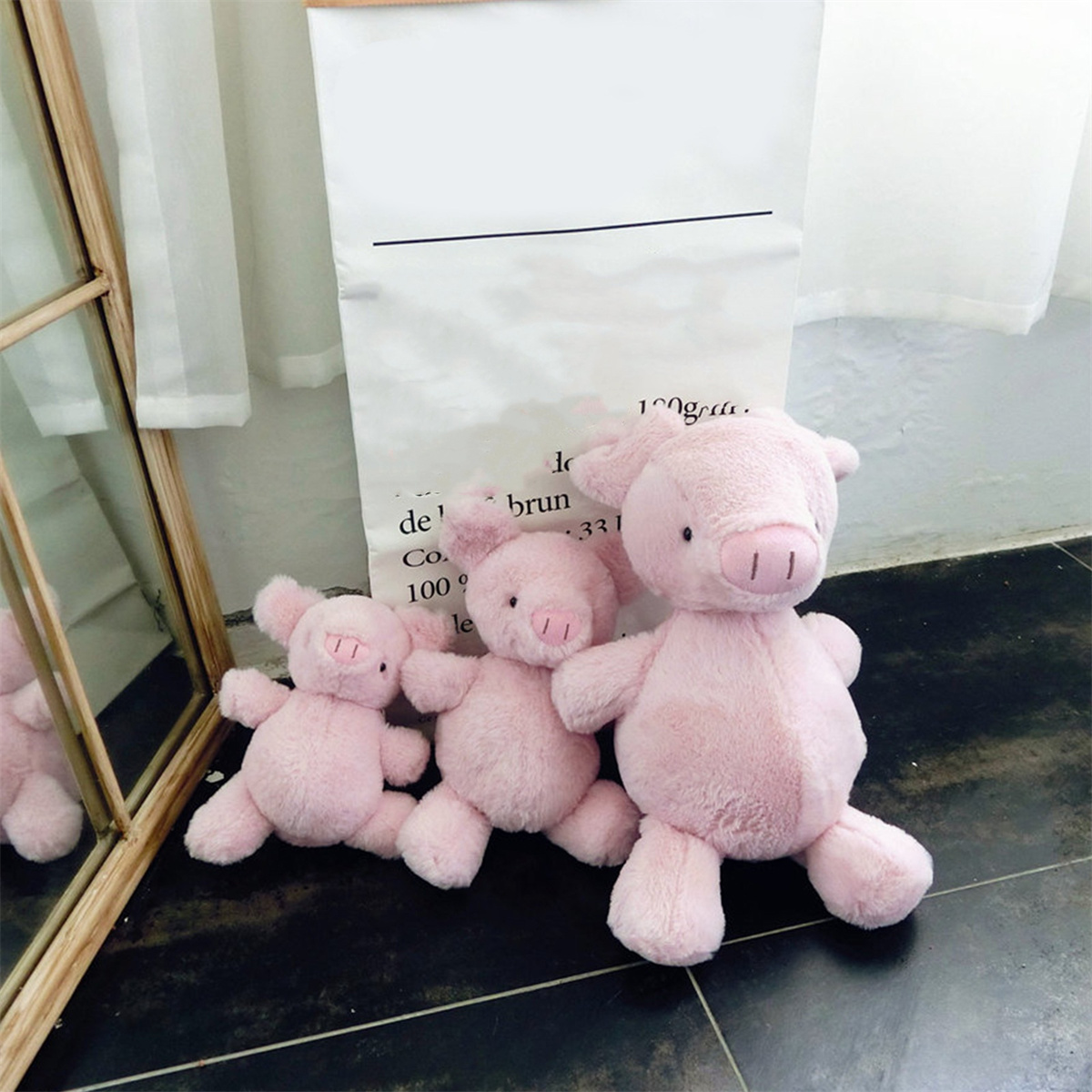 Drei rosa Schweine Stofftiere auf einem Fliesenboden. Im Hintergrund ist ein Spiegel.