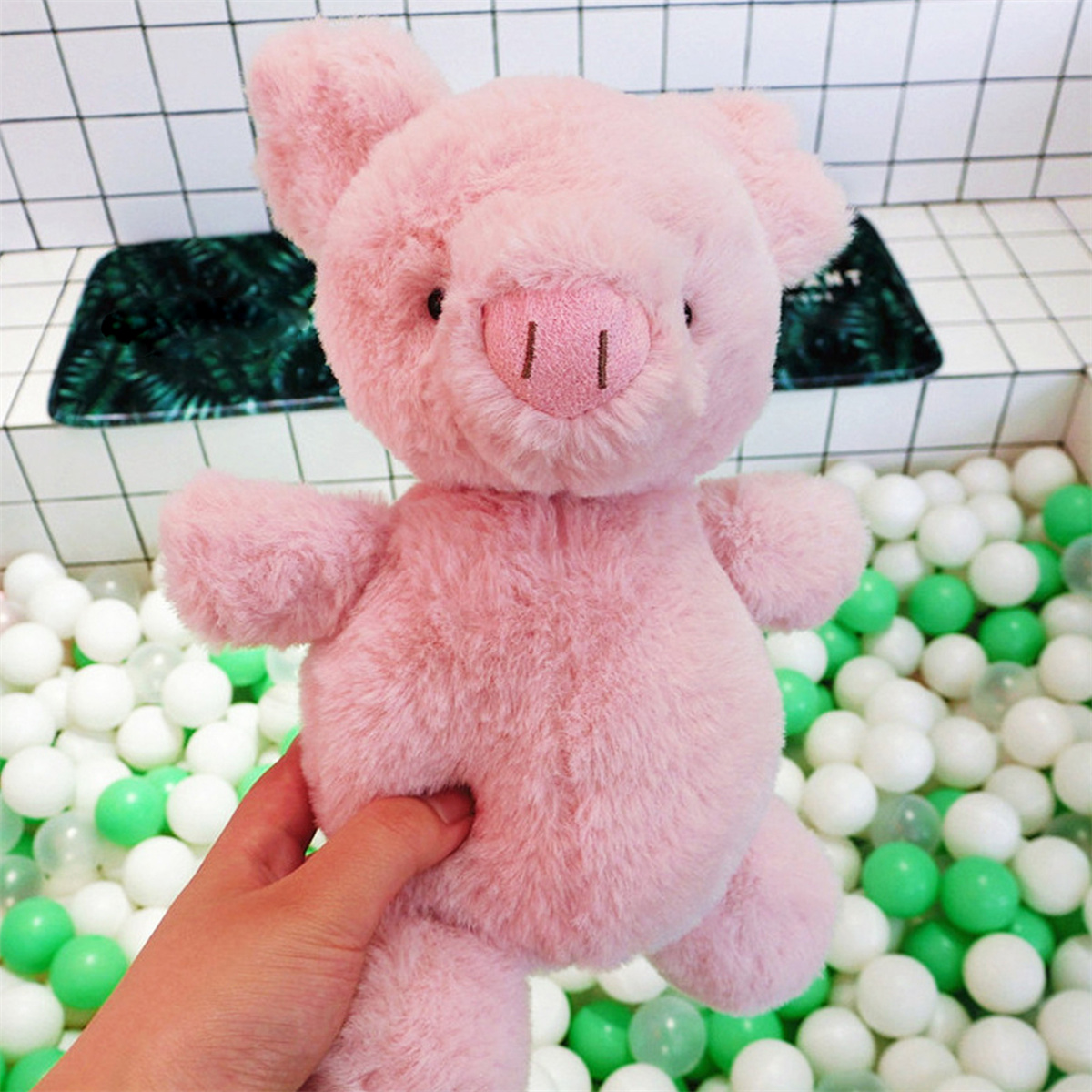 Rosa Plüschschwein-Spielzeug, das von einer Hand gehalten wird. Es befindet sich in einem Raum mit Bällen.