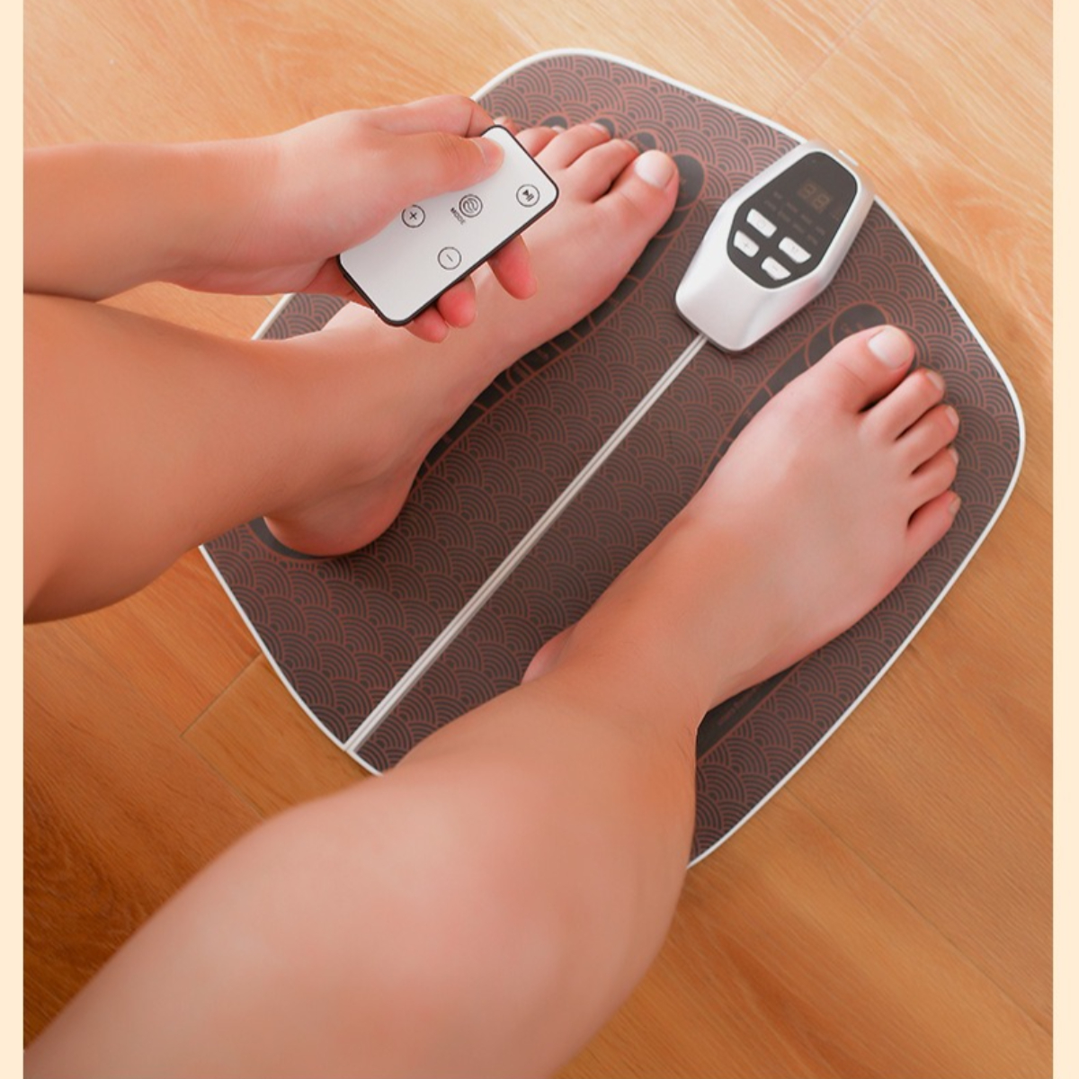 Füße einer Person auf einem braunen Fußmassagegerät. Eine Fernbedienung wird in der Hand gehalten. Holzfußboden.