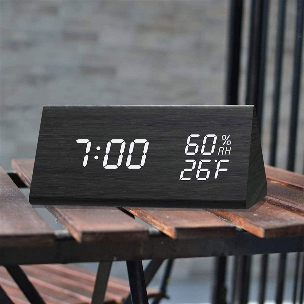 Eine schwarze digitale Holzuhr zeigt 7:00 Uhr, 60 % Luftfeuchtigkeit und 26 °F auf einem Tisch an.