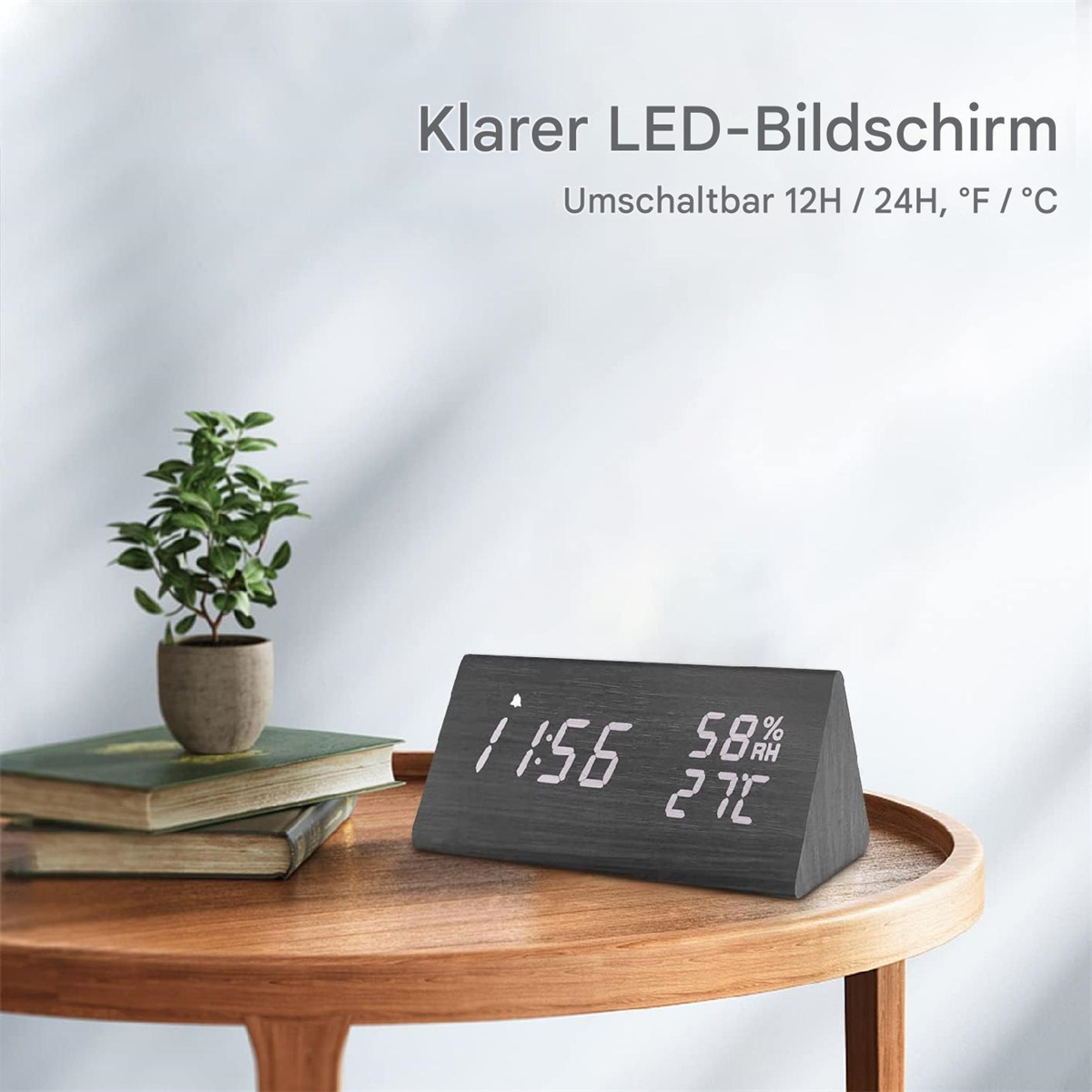 Holzuhr zeigt Zeit und Luftfeuchtigkeit. Eine kleine Pflanze und Bücher stehen auf einem Holztisch.