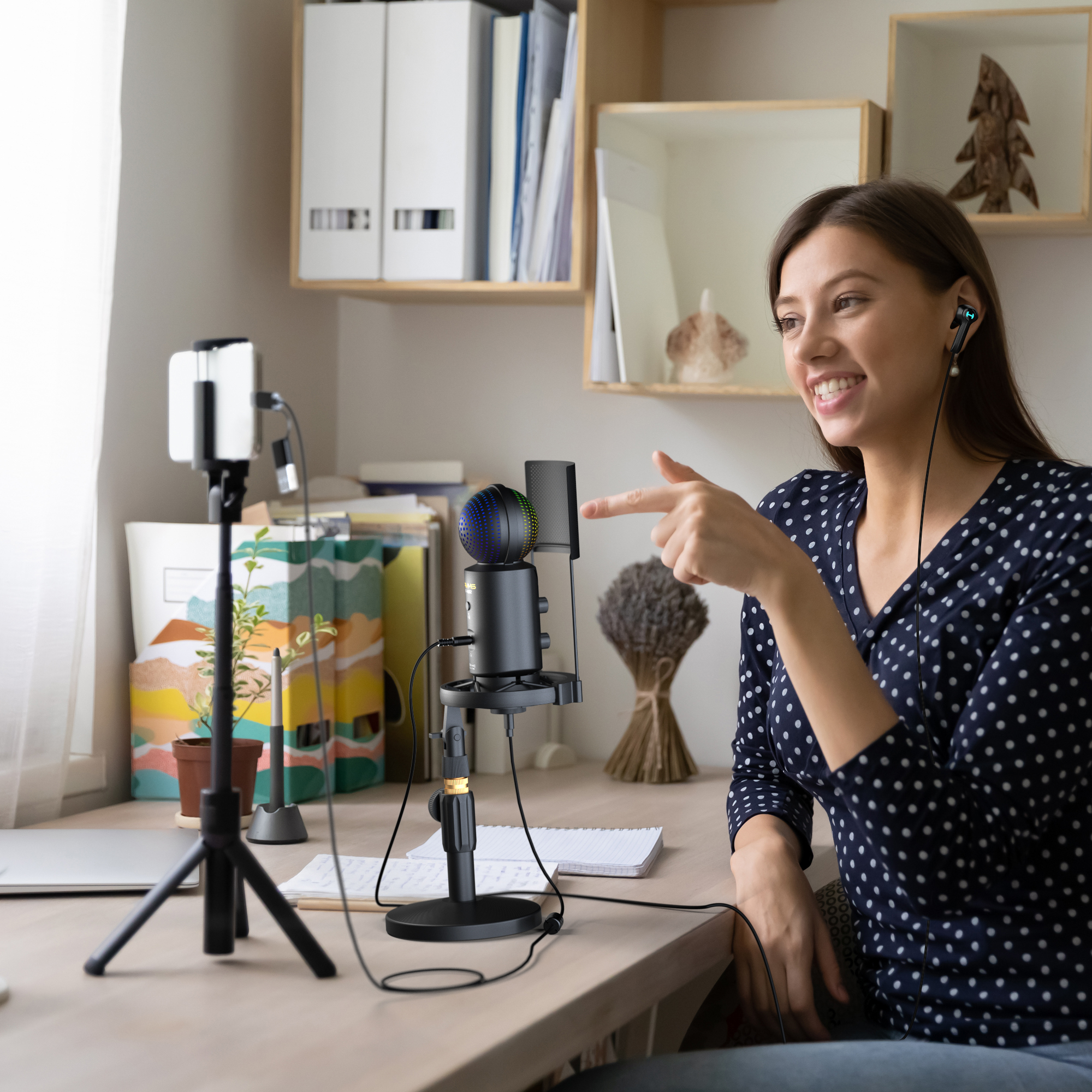 Een vrouw zit aan een bureau en praat in een microfoon met een telefoon.