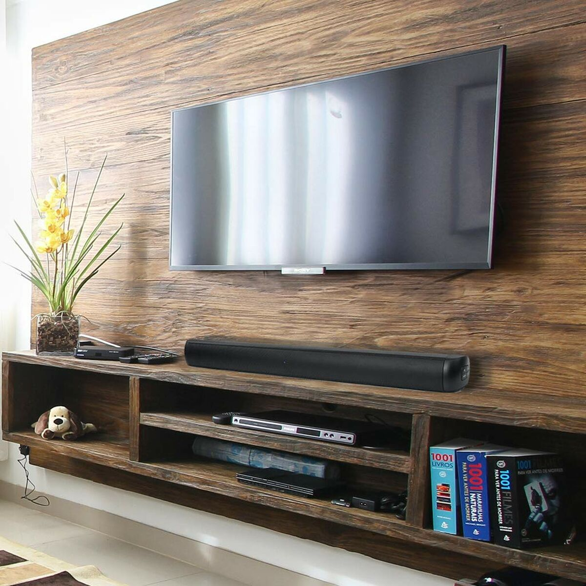 Parete in legno con TV montata, soundbar e mensole con decorazioni e libri.