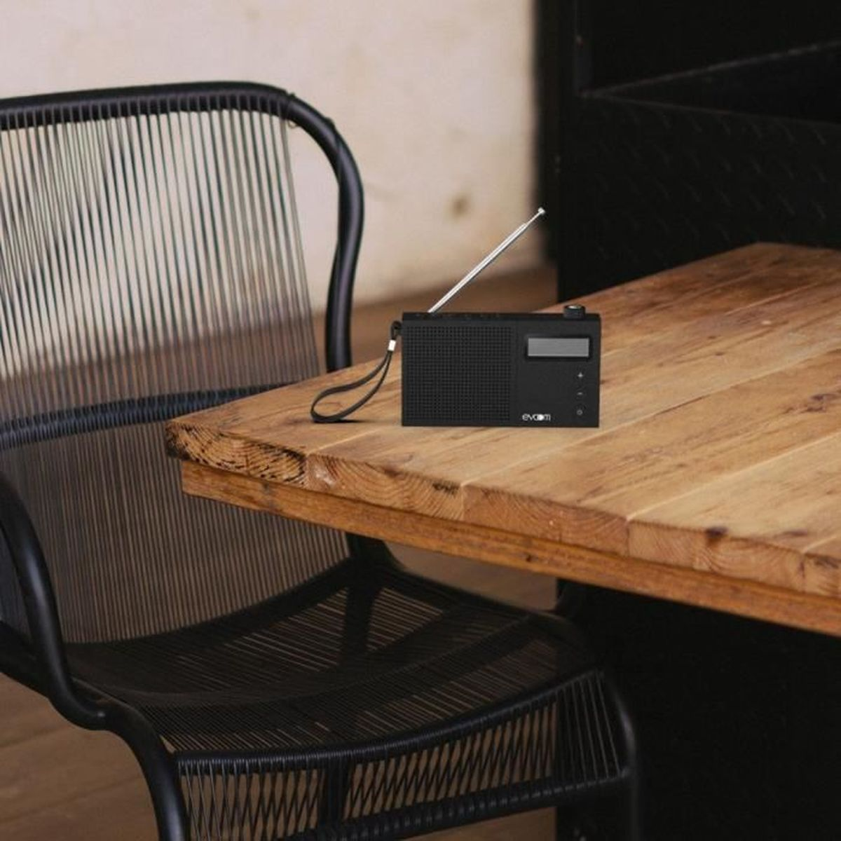Radio nera su un tavolo di legno. Una sedia nera a sinistra. Parete bianca sullo sfondo.