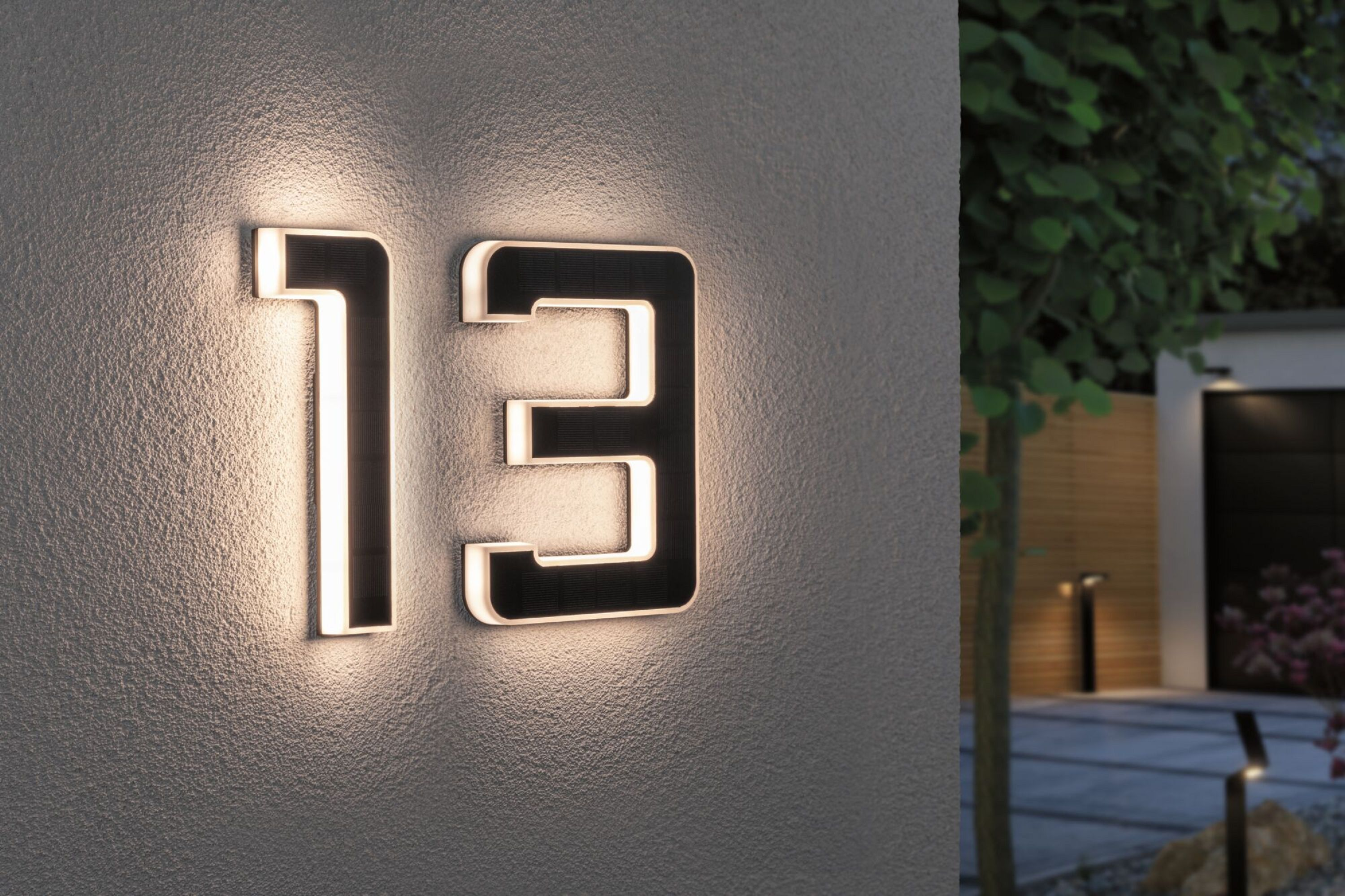 Podświetlony numer domu 13 na ścianie. Numery są czarne z białym blaskiem.