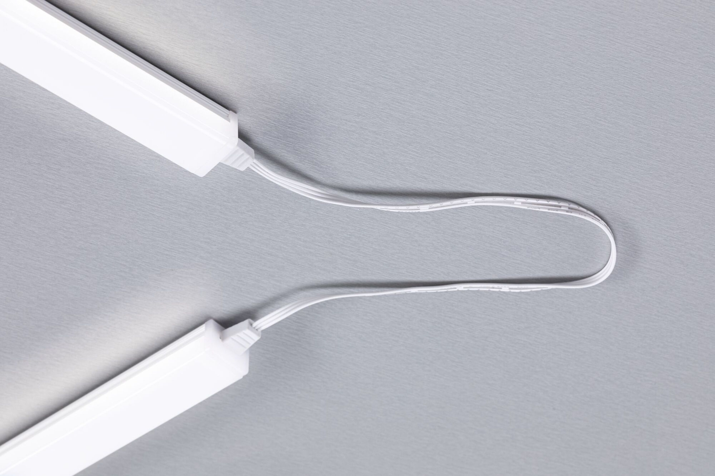Zwei weiße LED-Lichtleisten, die durch ein Kabel verbunden sind. Der Hintergrund ist eine graue Oberfläche.
