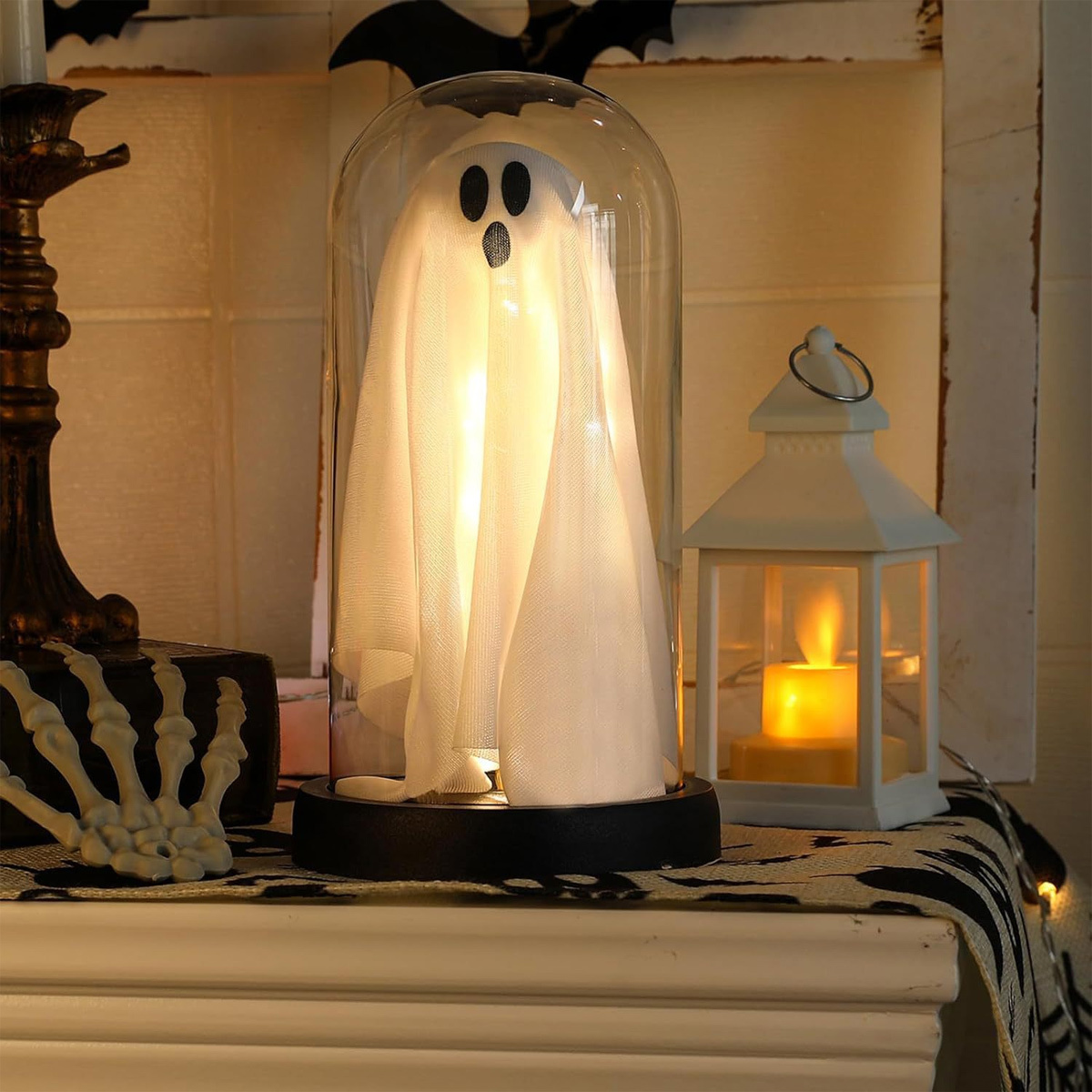 Eine Halloween-Dekoration: ein Geist unter einer Glaskuppel, mit einer Laterne und einer gruseligen Skeletthand.