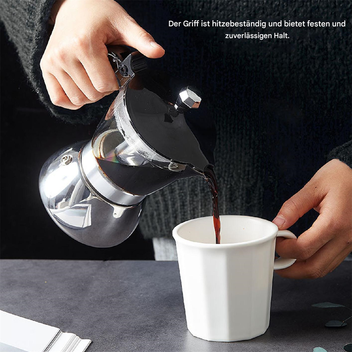 Eine Person gießt Kaffee aus einem silbernen Espressokocher in eine weiße Tasse. Der Griff ist hitzebeständig.
