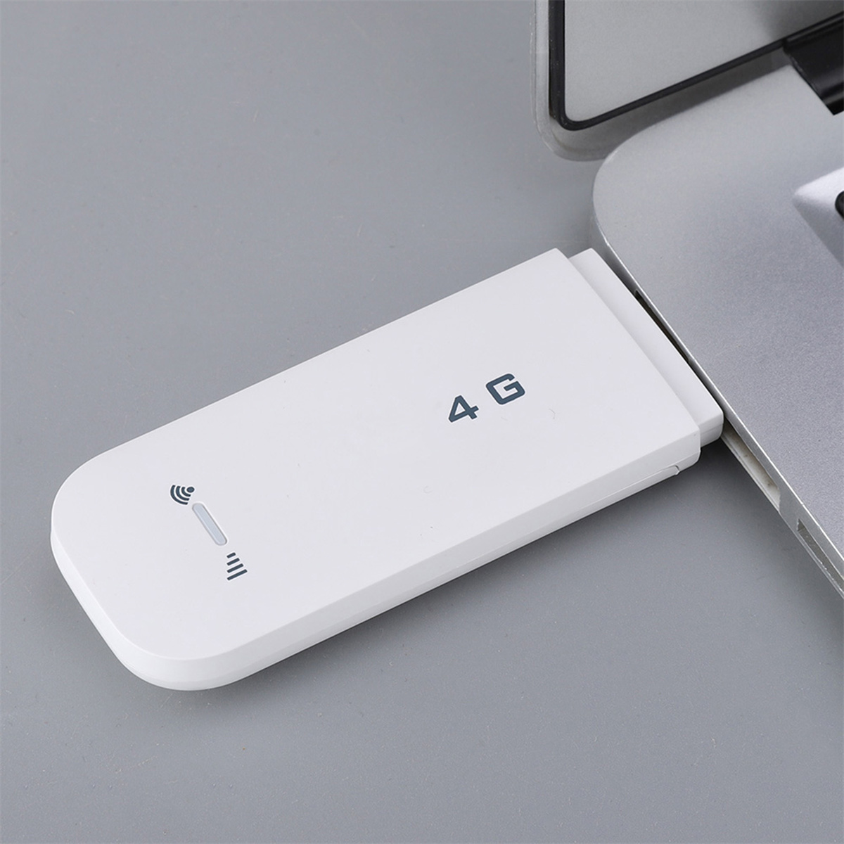 Ein weißes 4G-Modem ist mit einem Laptop verbunden. Es liegt auf einer grauen Oberfläche.