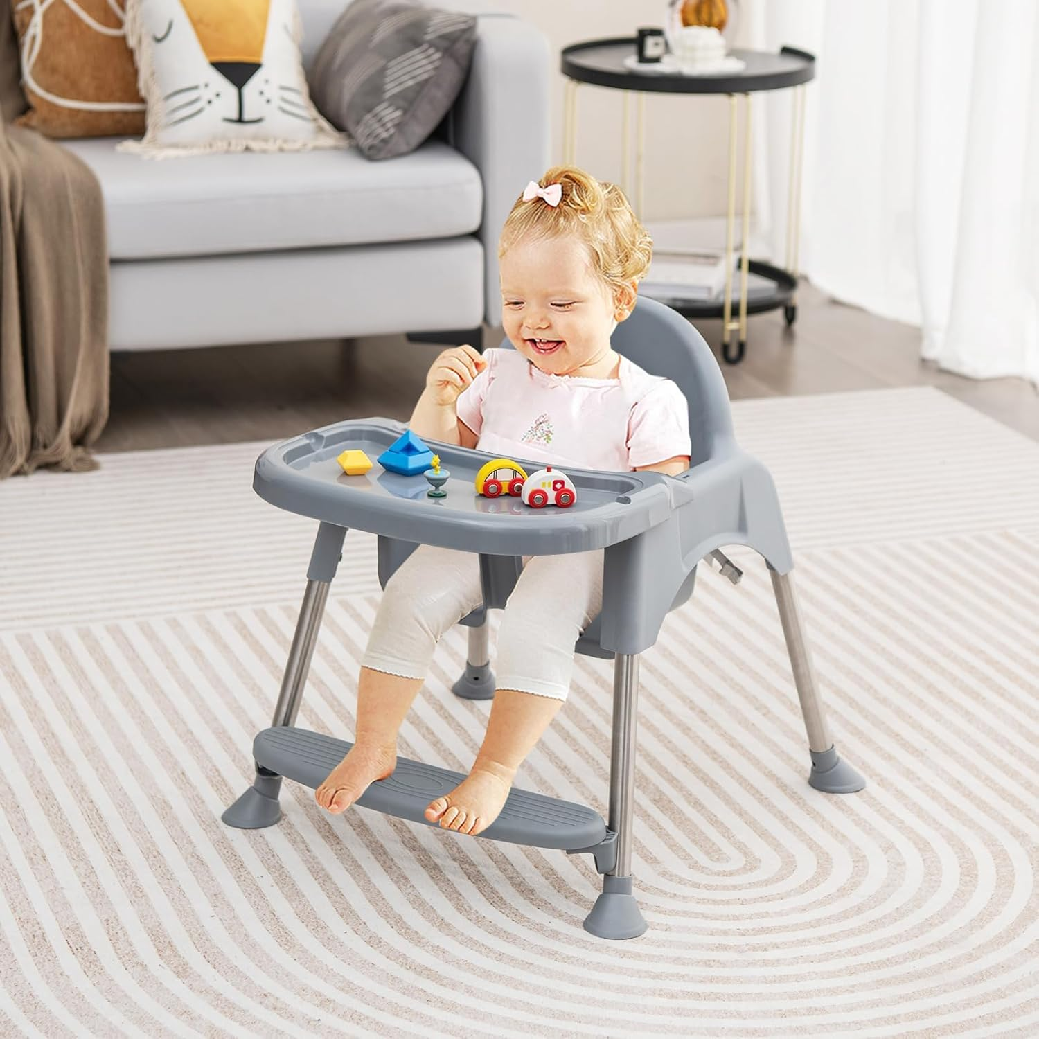 Ein Baby sitzt in einem grauen Hochstuhl mit Spielzeug auf dem Tablett.