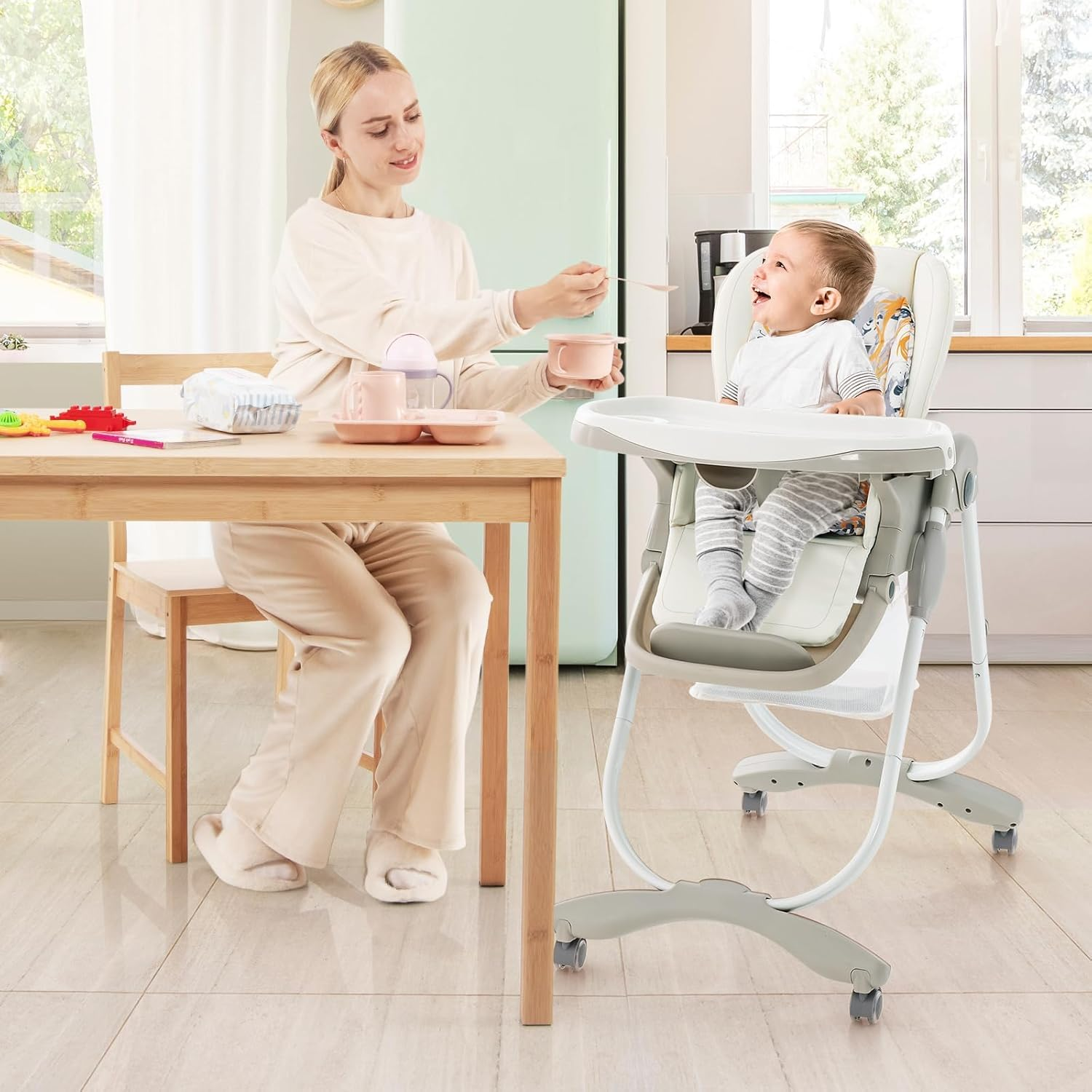 Mutter füttert Baby im Hochstuhl. Küchenumgebung. Rosa Schüssel und Esstisch.