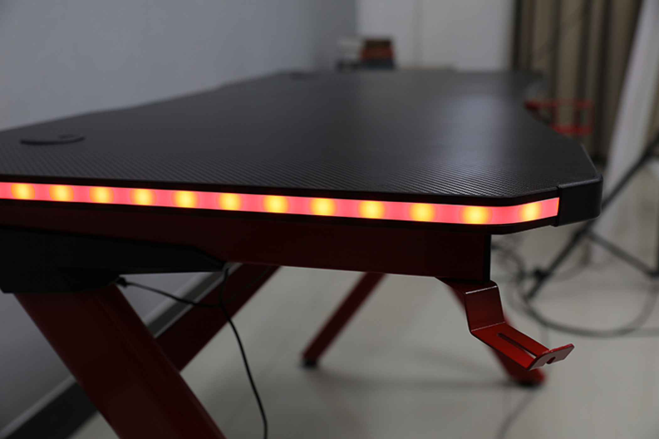 Ein Gaming-Schreibtisch mit roten Beinen, einer schwarzen Oberseite und roter LED-Beleuchtung am Rand.