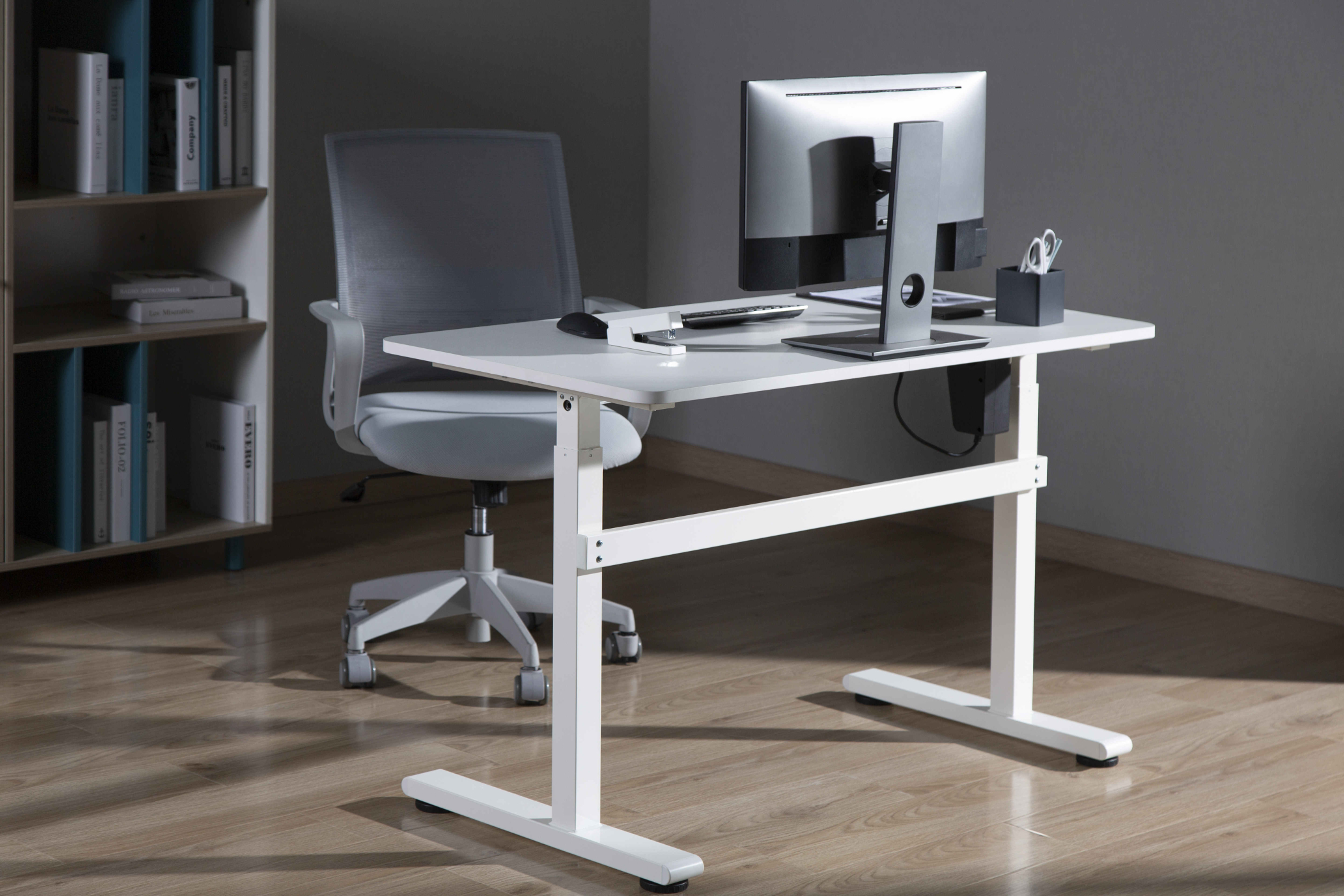 Witte bureau met monitor, stoel en boekenplank op de achtergrond.