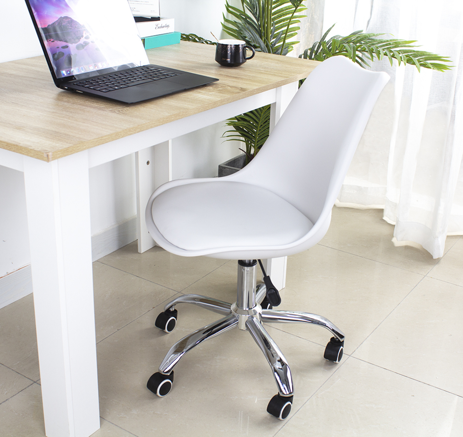 White office chair with wheels next to a wooden desk with a laptop and a plant.