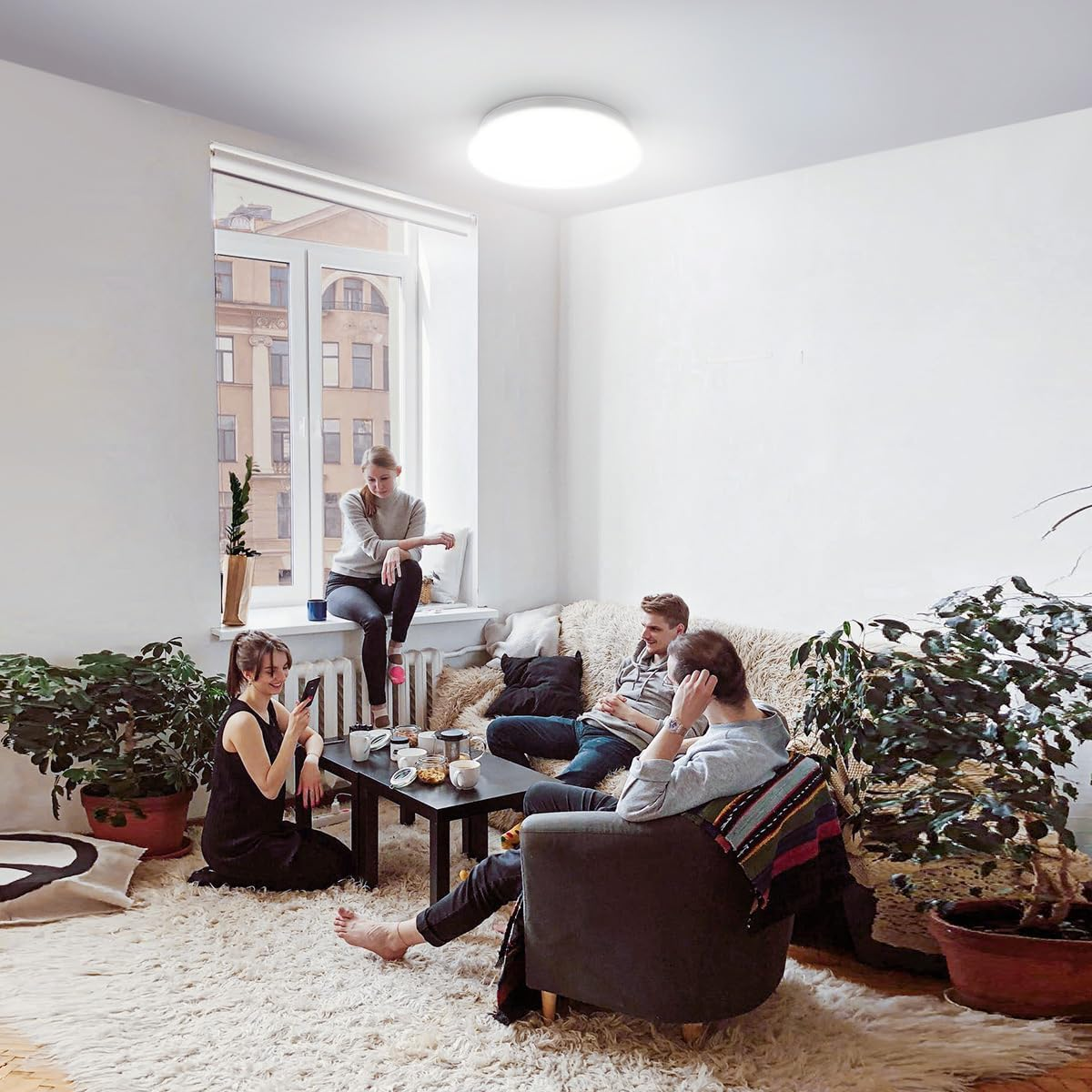 Vier Personen in einem Wohnzimmer. Sie sitzen auf einem Sofa, dem Boden und einem Fensterplatz.