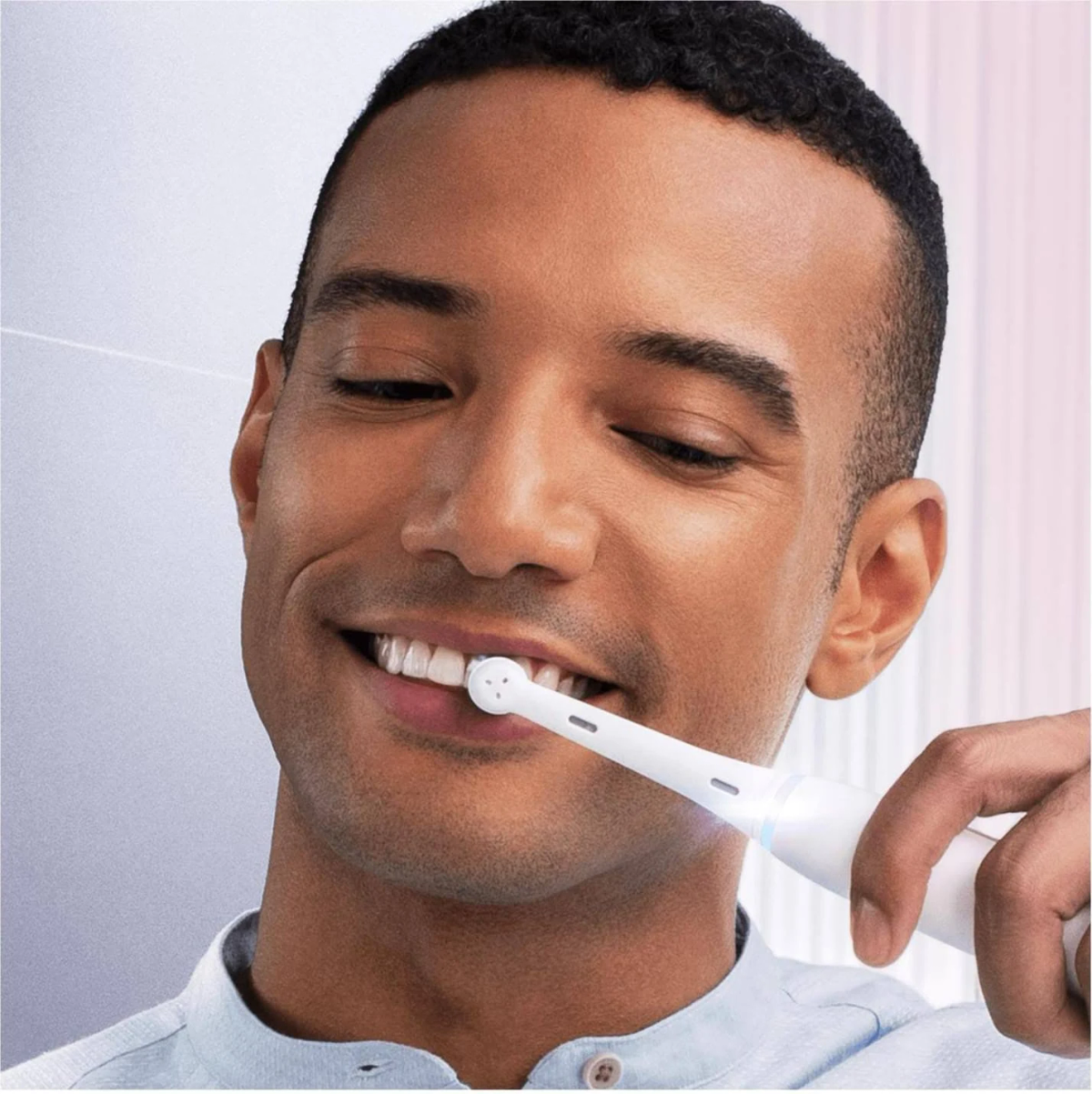 Uomo che usa uno spazzolino elettrico, sorridendo. Lo spazzolino è bianco.