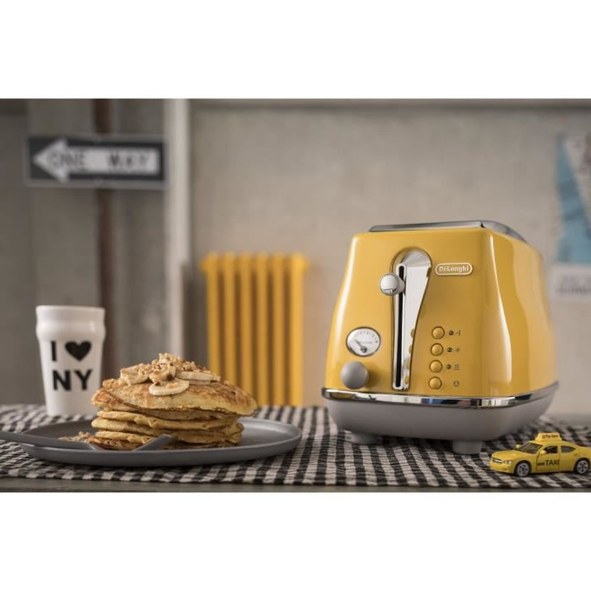 Gele broodrooster met pannenkoeken, siroop en een speelgoedtaxi op een geruit tafelkleed.