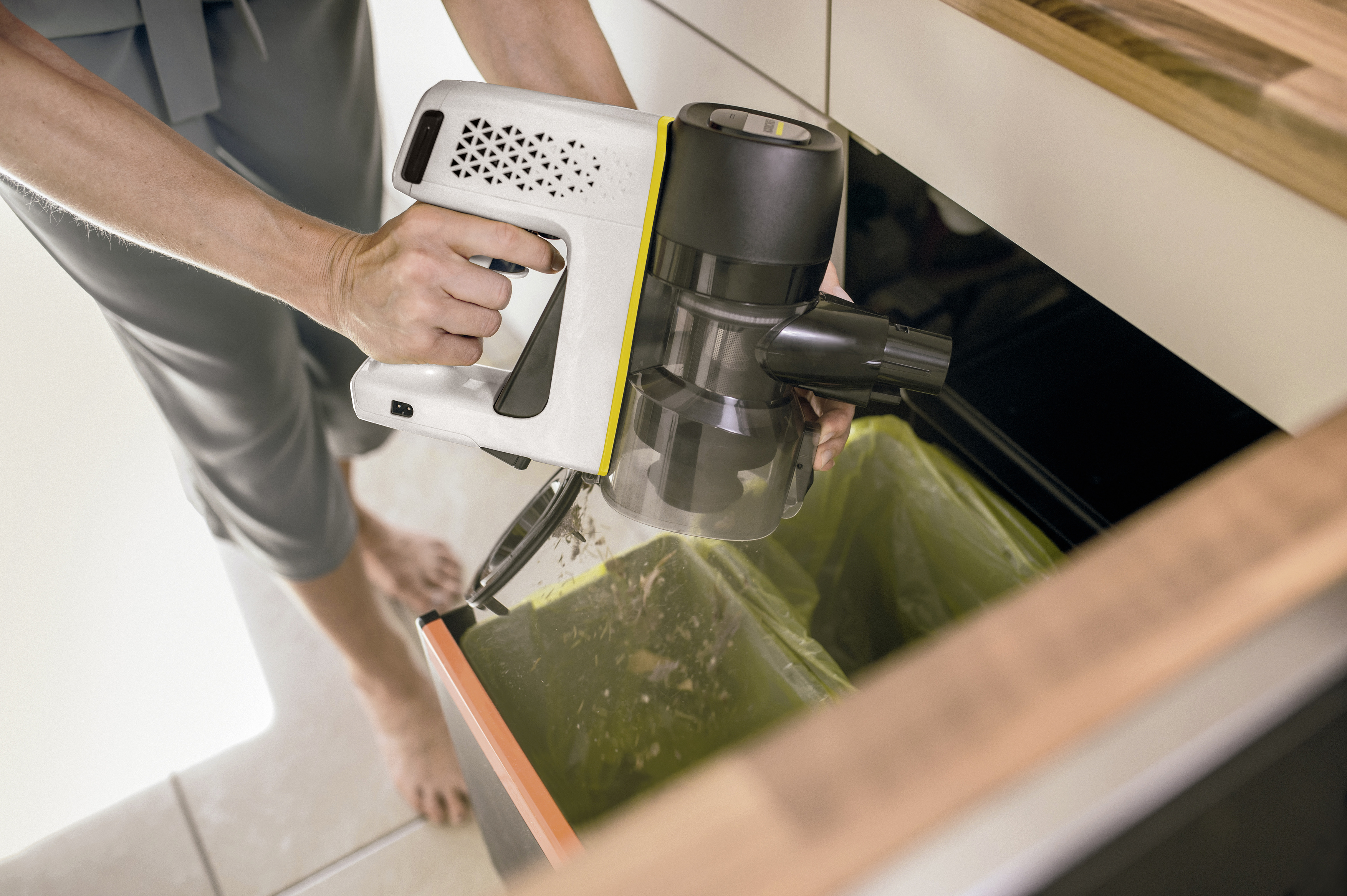 A person holds a white and black handheld vacuum over a trash bin, discarding waste.