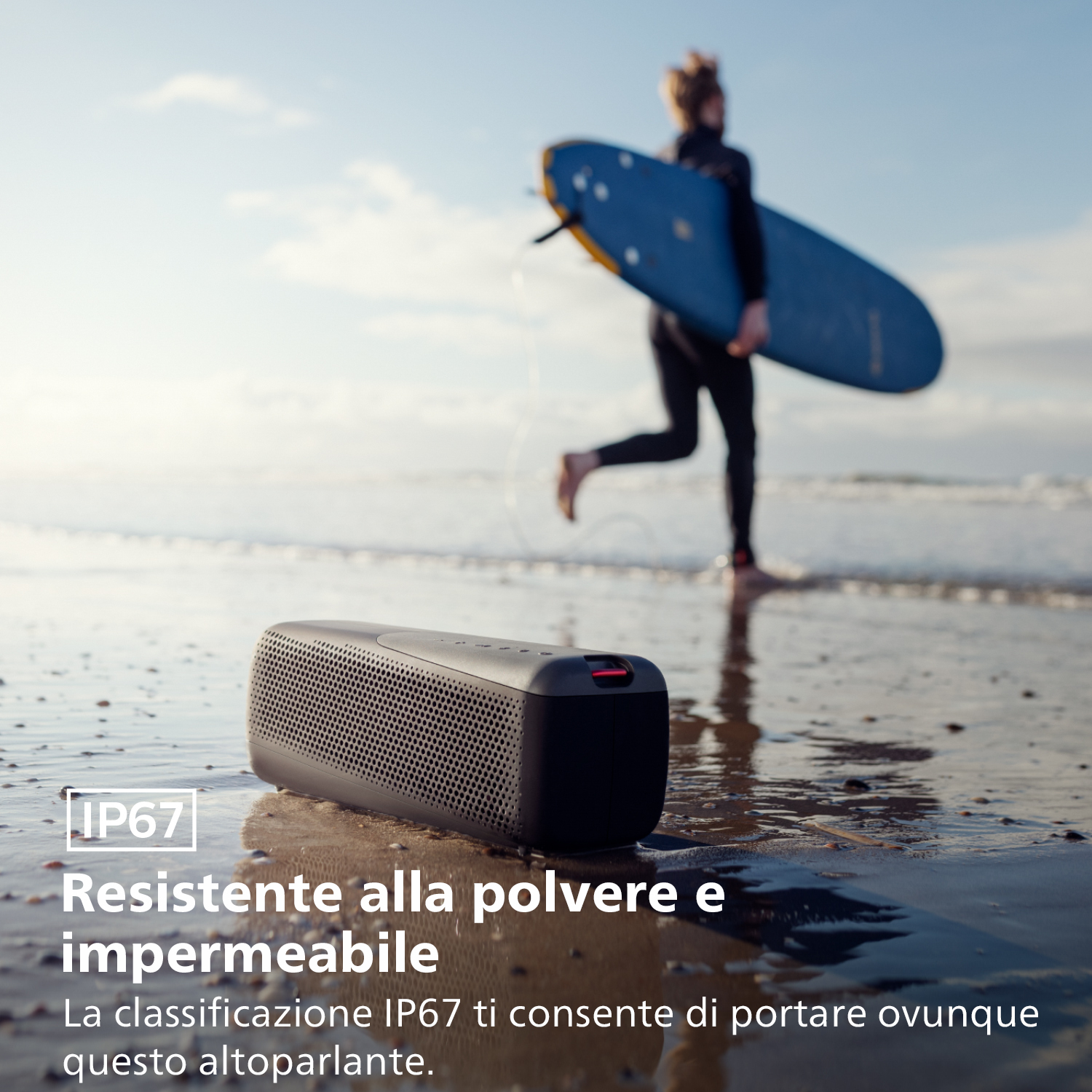 Czarny głośnik na plaży z tekstem. Surfer idzie w tle z deską surfingową.