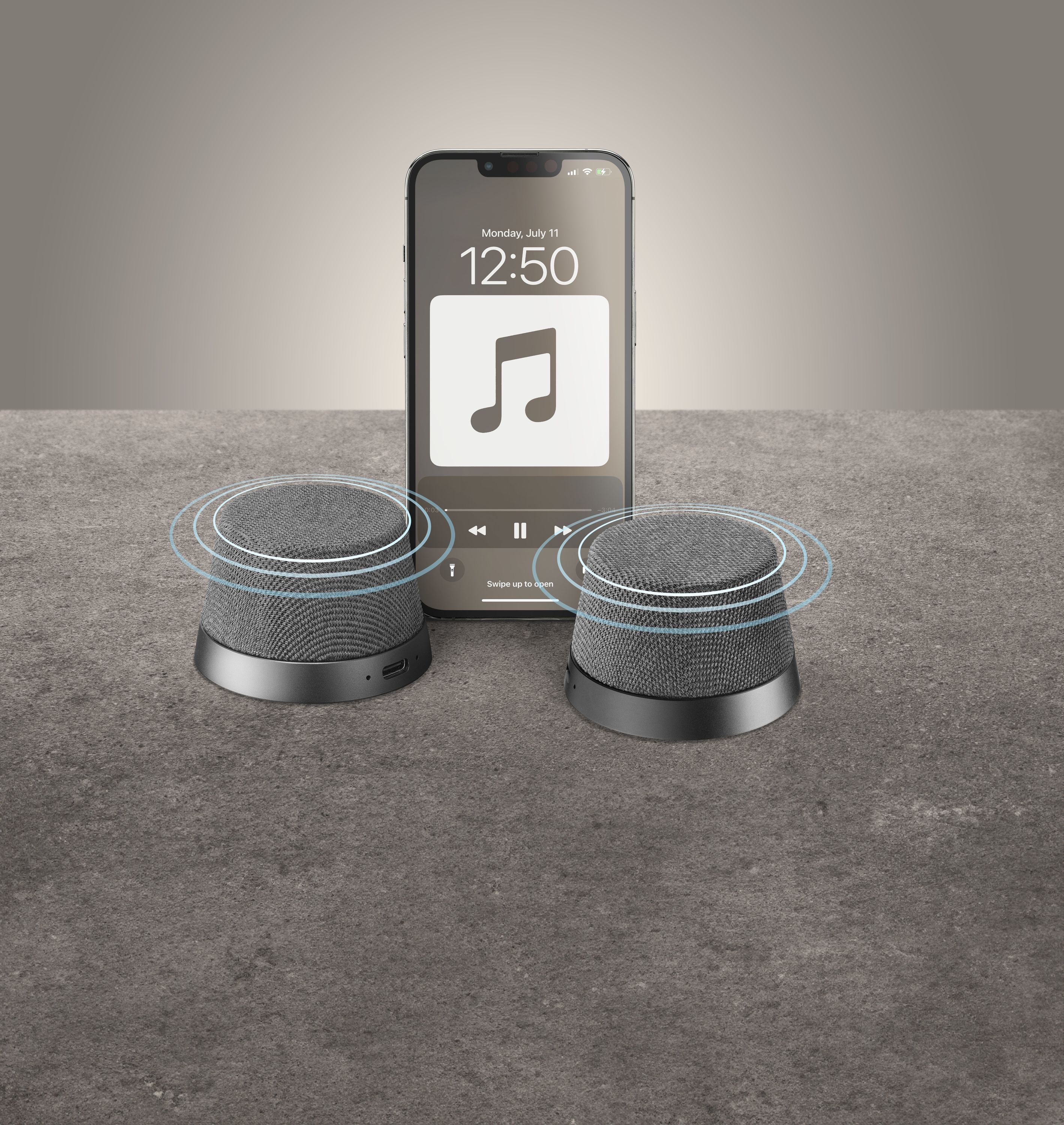 Zwei schwarze Lautsprecher und ein Telefon mit Musikoberfläche liegen auf grauer Fläche.