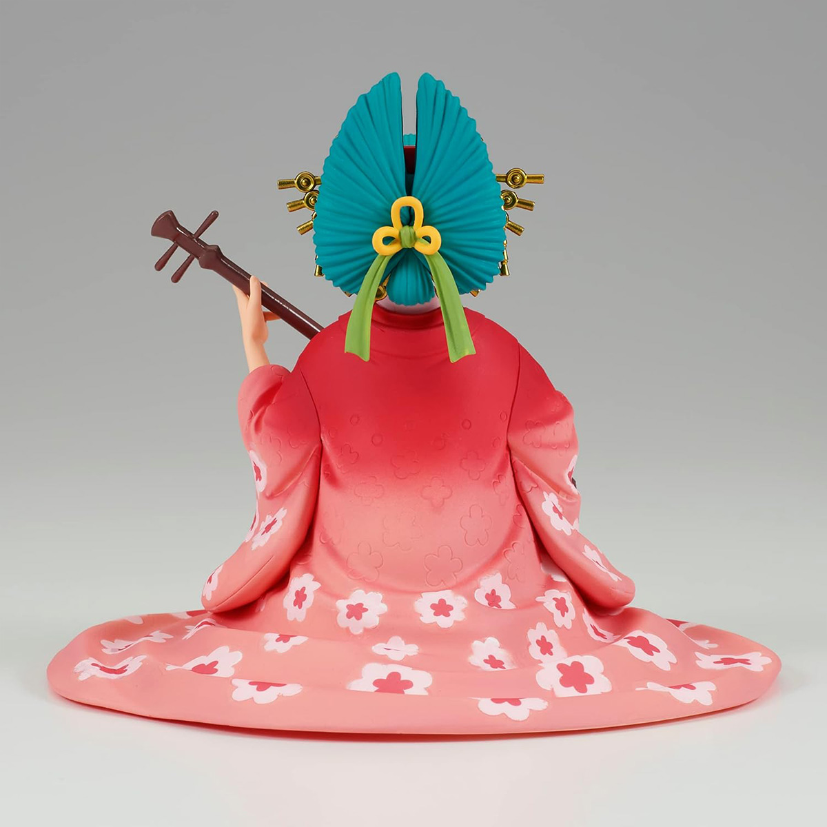 Vista trasera de una figura con tocado turquesa, kimono rosa, sosteniendo un instrumento de cuerda.