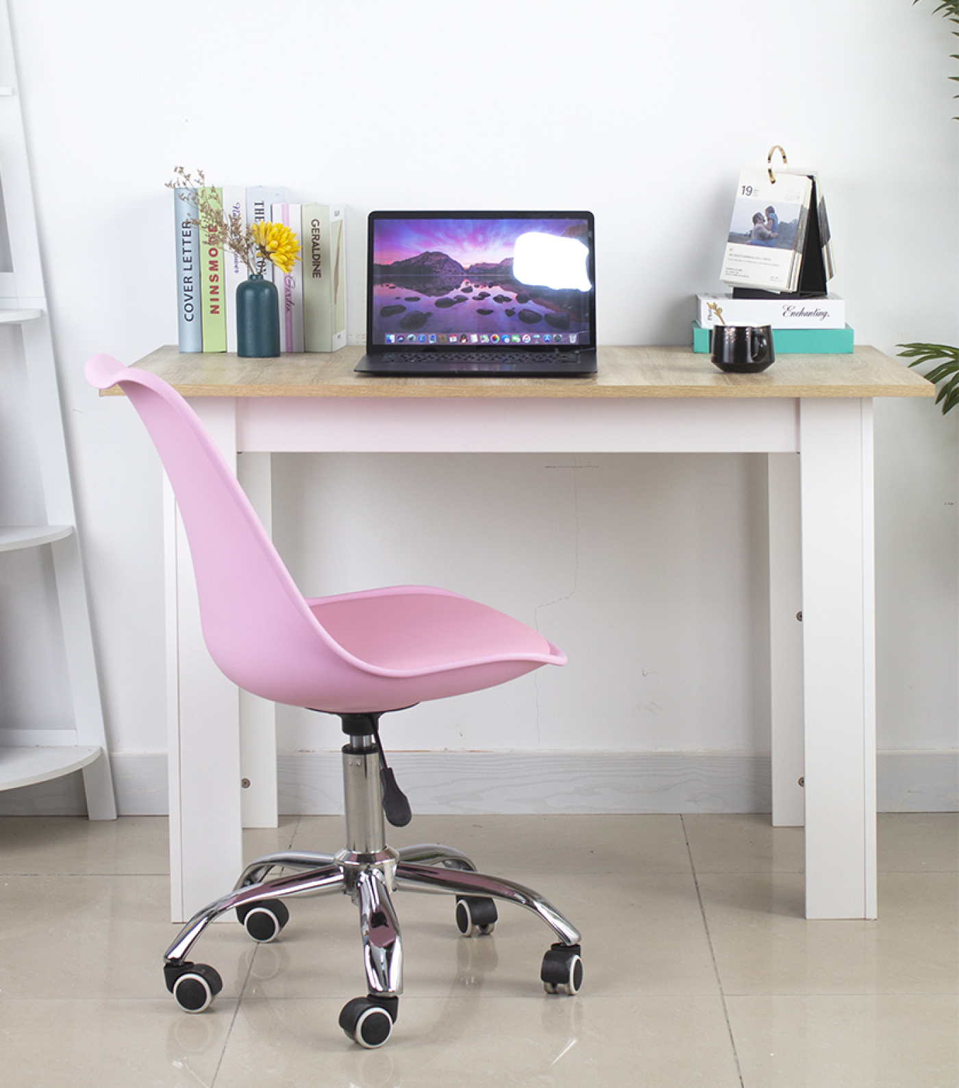 A pink chair and a wooden desk with a laptop, books, and a calendar. White wall background.