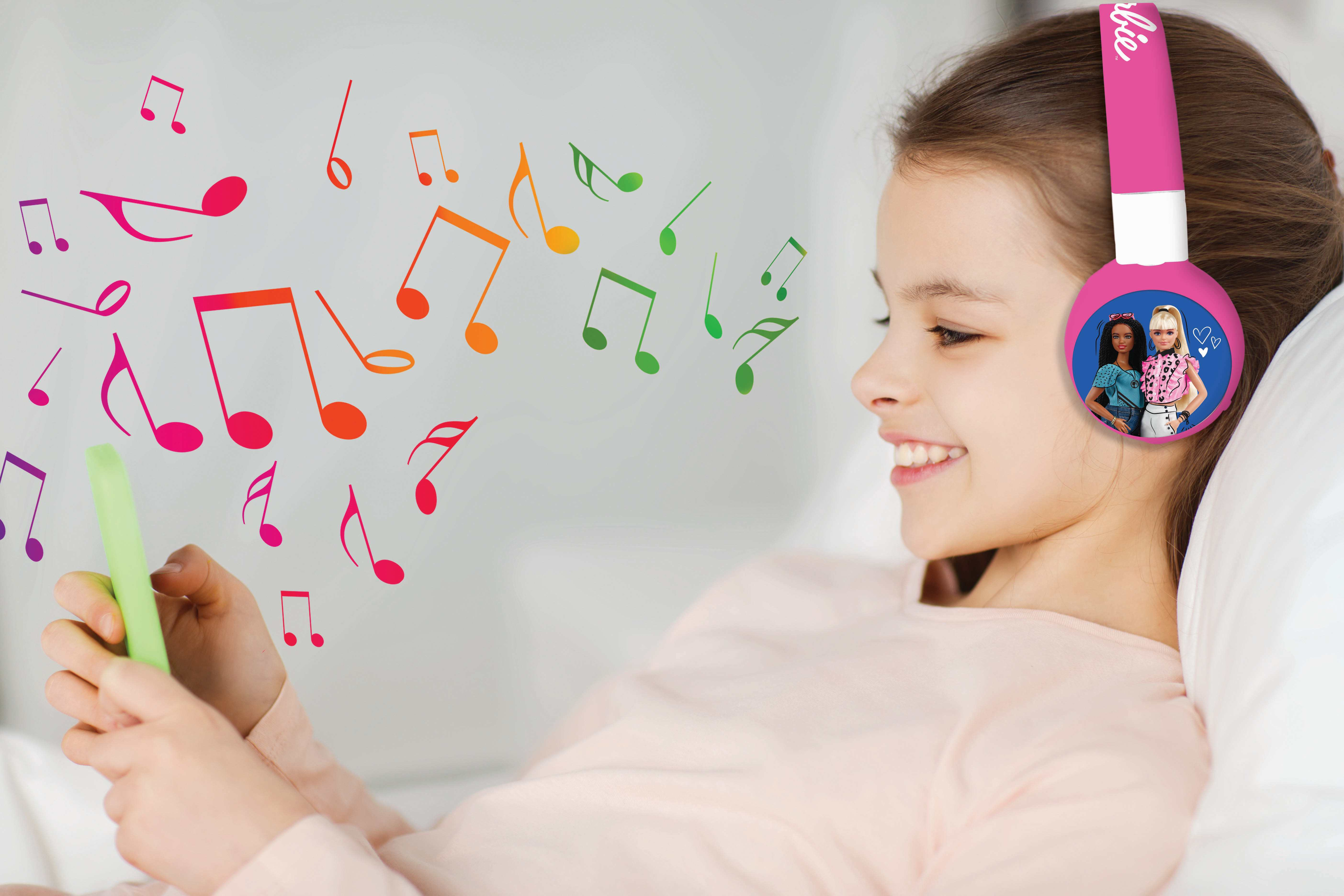 Una niña sonríe, usando auriculares rosas con imagen de Barbie.