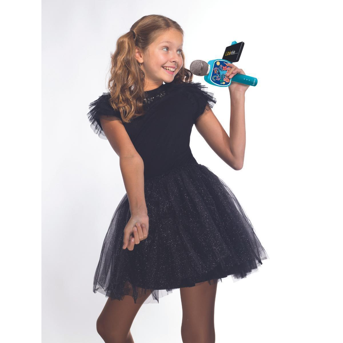 Młoda dziewczyna w czarnej sukience z mikrofonem do karaoke, uśmiechnięta i odwracająca wzrok.