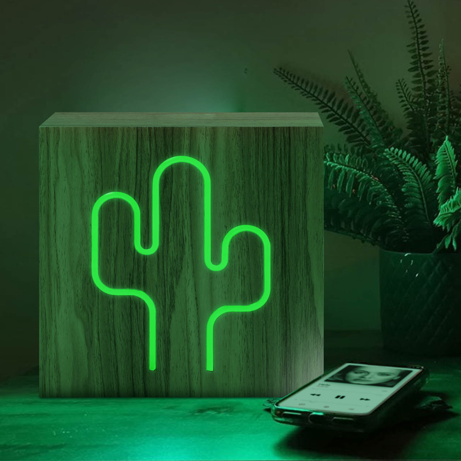 Bloc de bois avec un cactus vert néon. Téléphone sur la table. Fond vert.