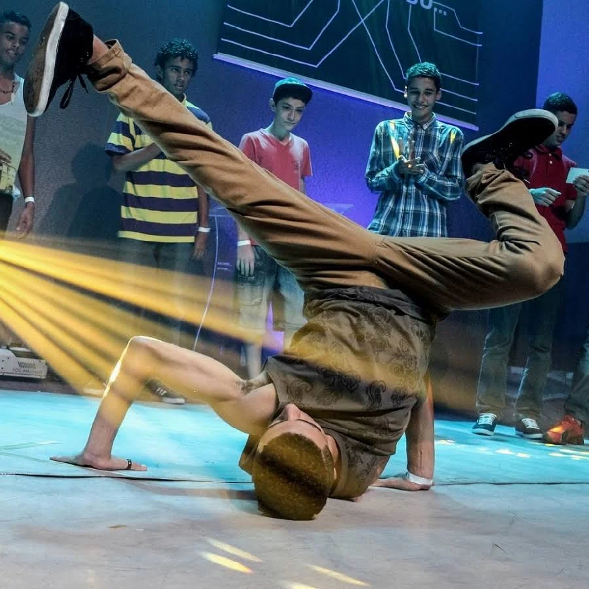 Un uomo in posizione di handstand sul palco, circondato da persone.