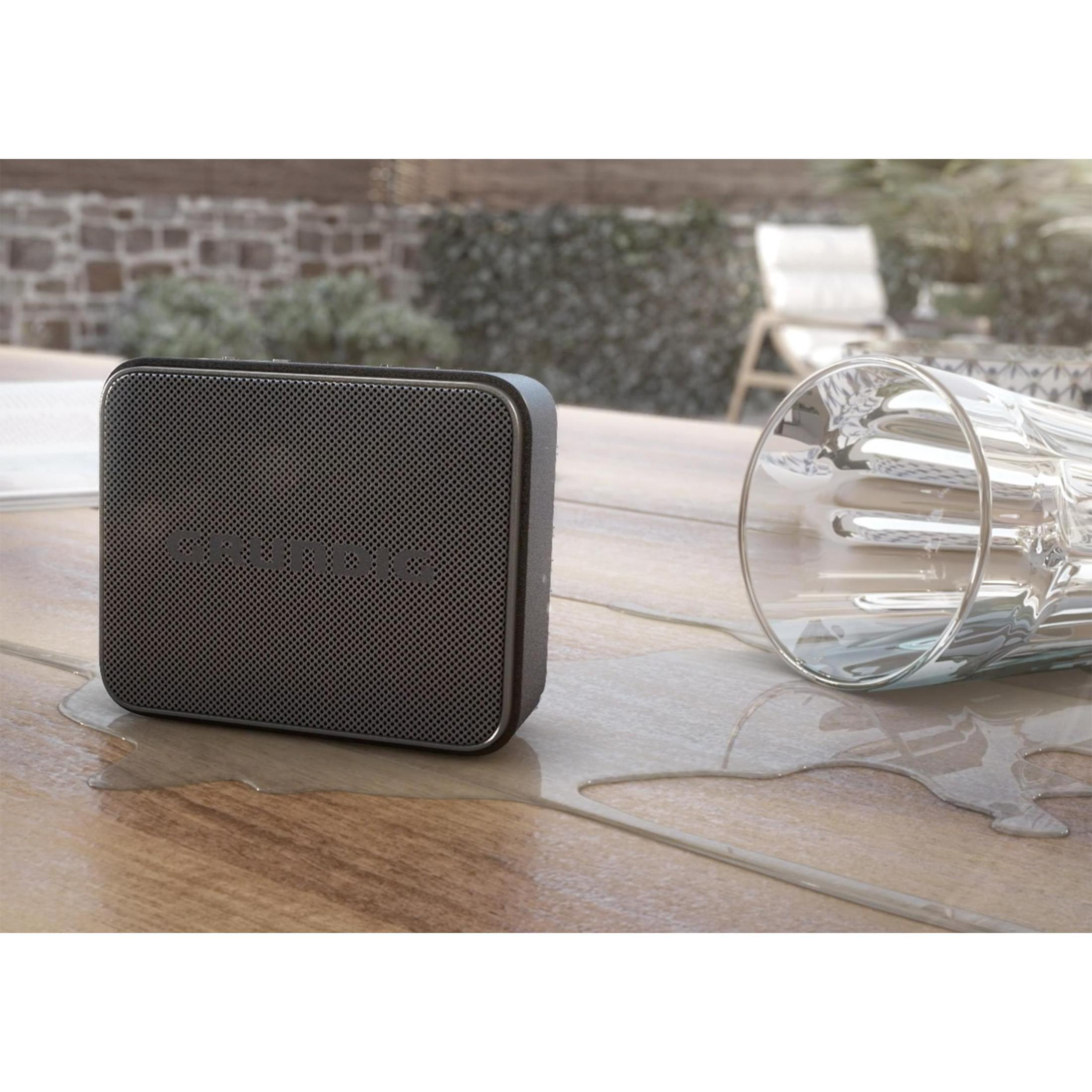 Czarny głośnik na drewnianym stole. Szklanka obok głośnika. Woda na stole.