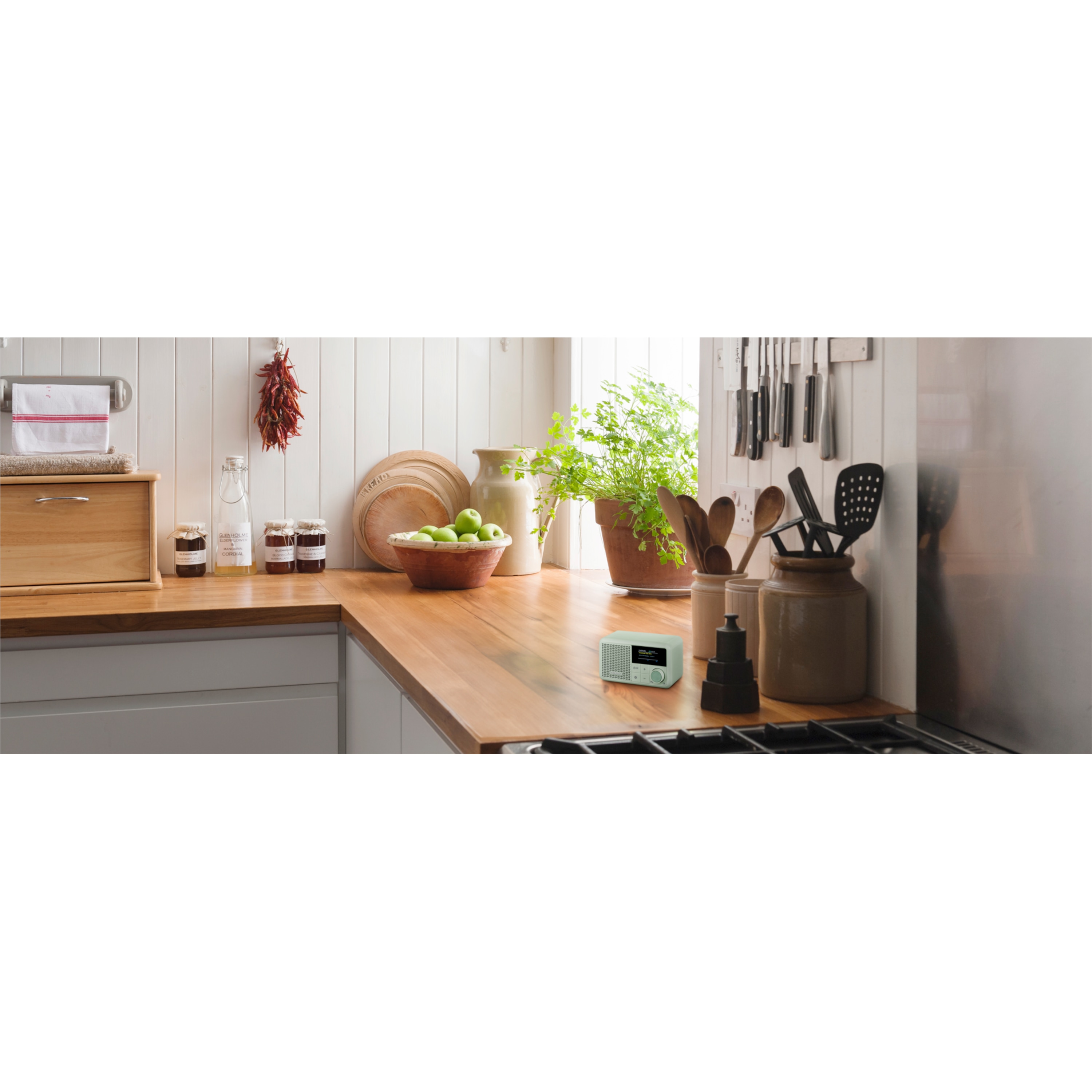 A kitchen counter with various items: a wooden breadbox, jars, dishes, a plant, utensils, and a radio.