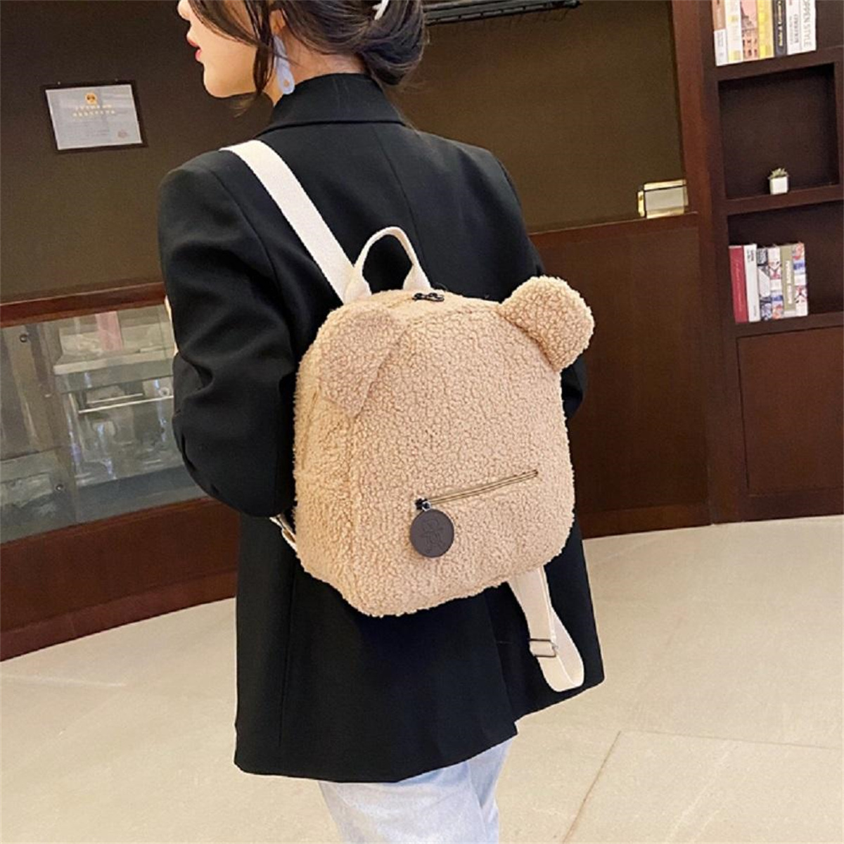 Eine Frau mit schwarzer Jacke und einem teddybärförmigen Rucksack mit weißen Trägern.